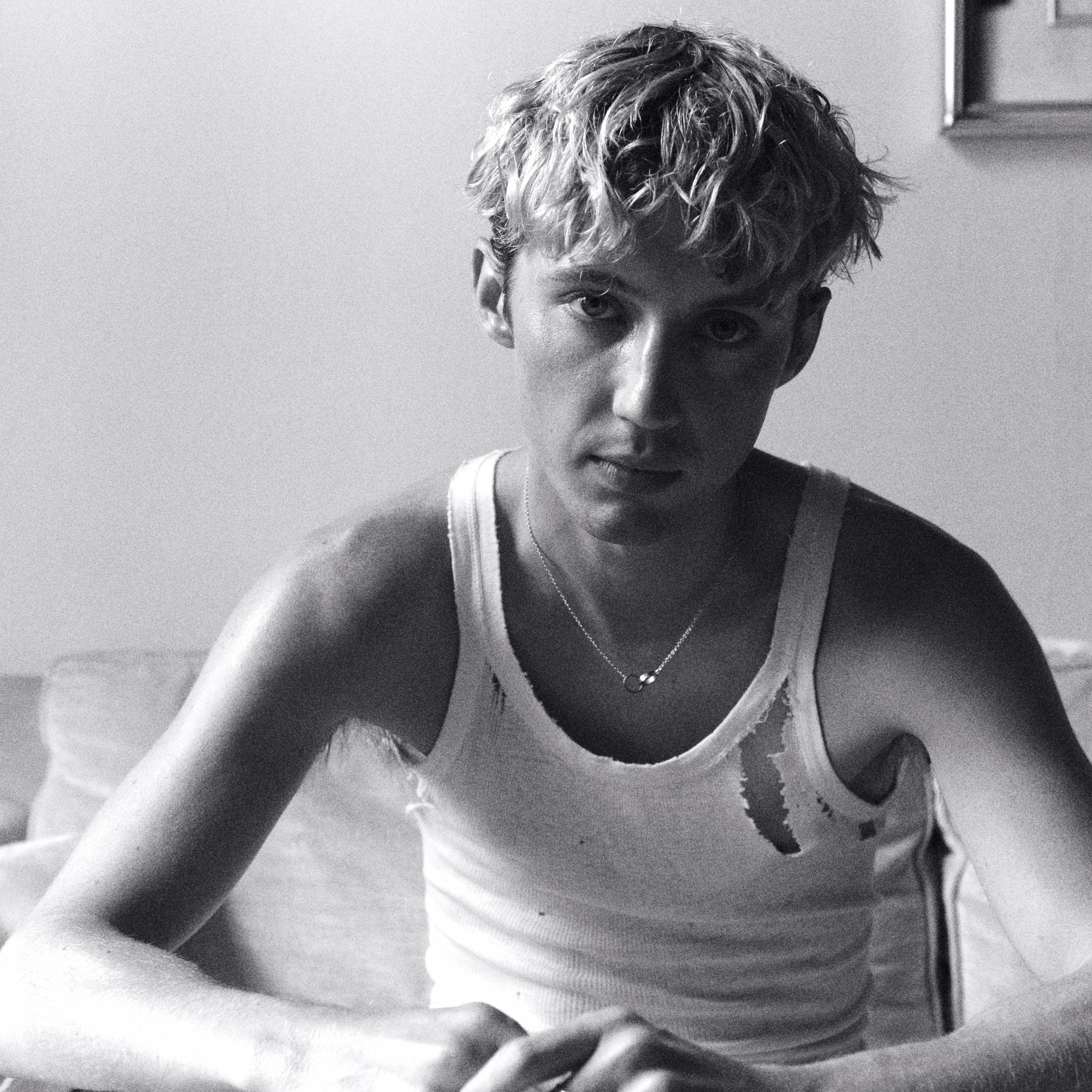 A black and white photo of Troye Sivan in a ripped tank top