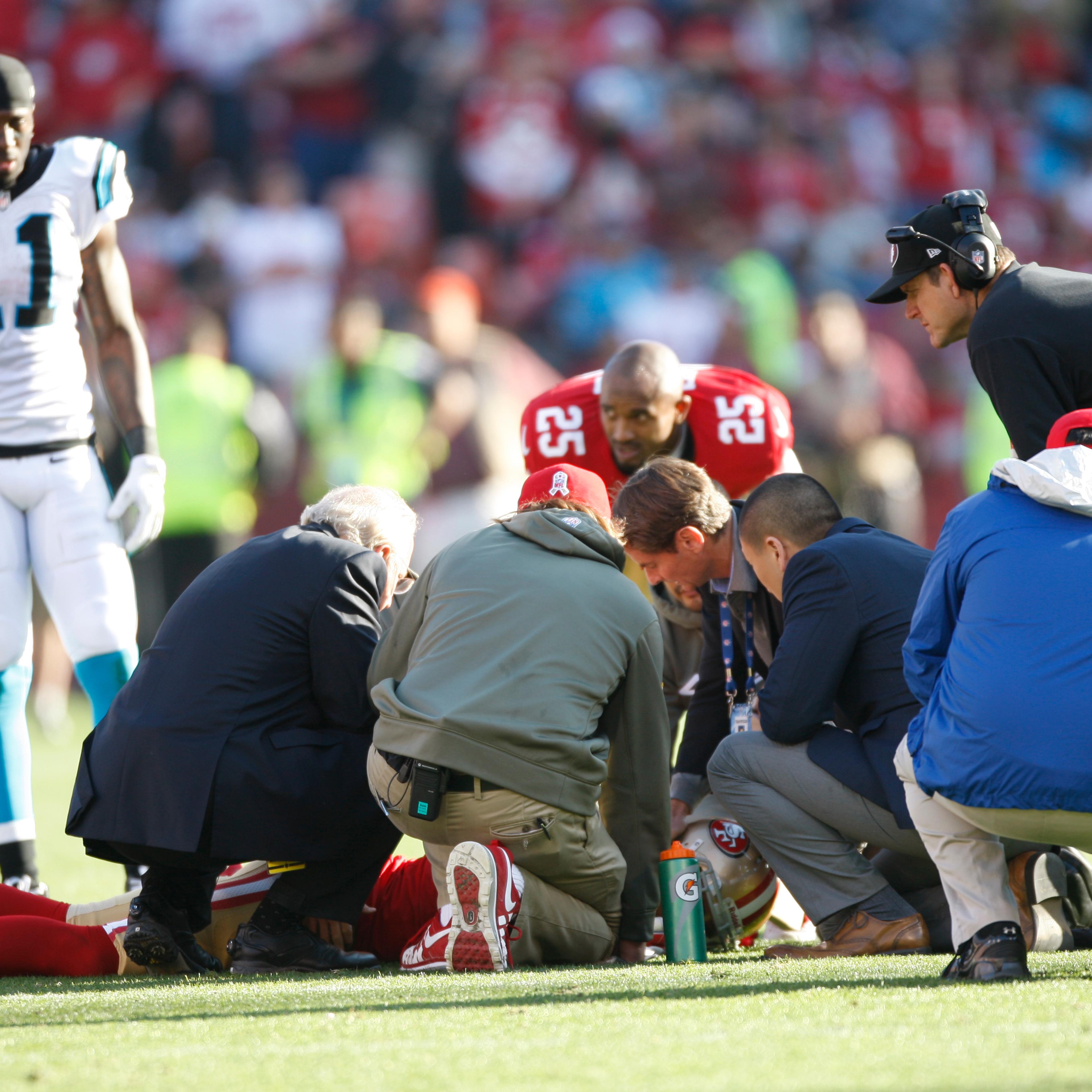 From left: Head Coach Jim Harbaugh of the San Francisco 49ers and the medical staff check out Eric Reid after he received a concussion during the game against the Carolina Panthers on November 10, 2013 in San Francisco, California.