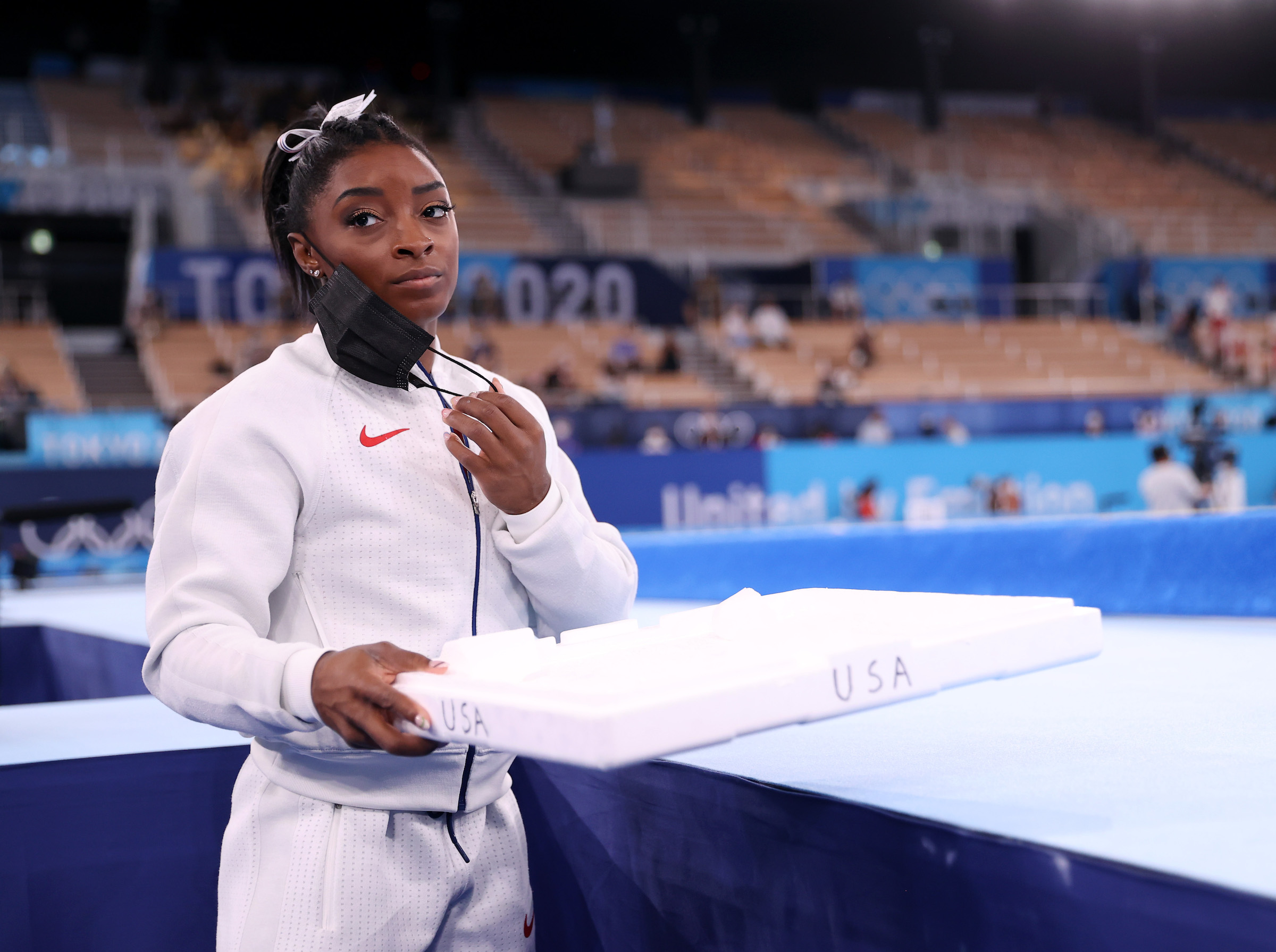 Simone Biles of Team United States supports her team mates by carrying their chalk after pulling out after the vault during the Women's Team Final on day four on day four of the Tokyo 2020 Olympic Games at Ariake Gymnastics Centre on July 27, 2021 in Tok