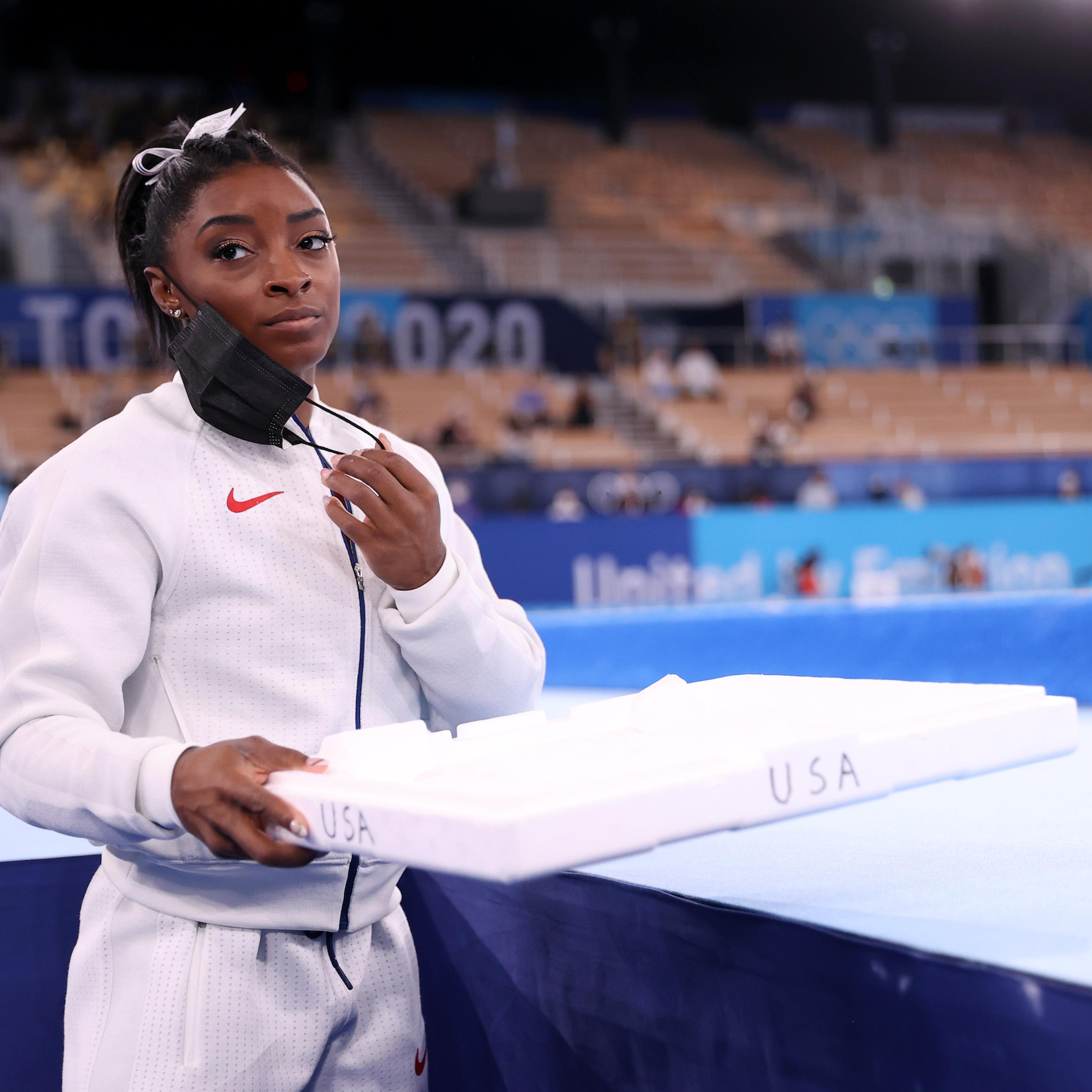 Simone Biles of Team United States supports her team mates by carrying their chalk after pulling out after the vault during the Women's Team Final on day four on day four of the Tokyo 2020 Olympic Games at Ariake Gymnastics Centre on July 27, 2021 in Tok
