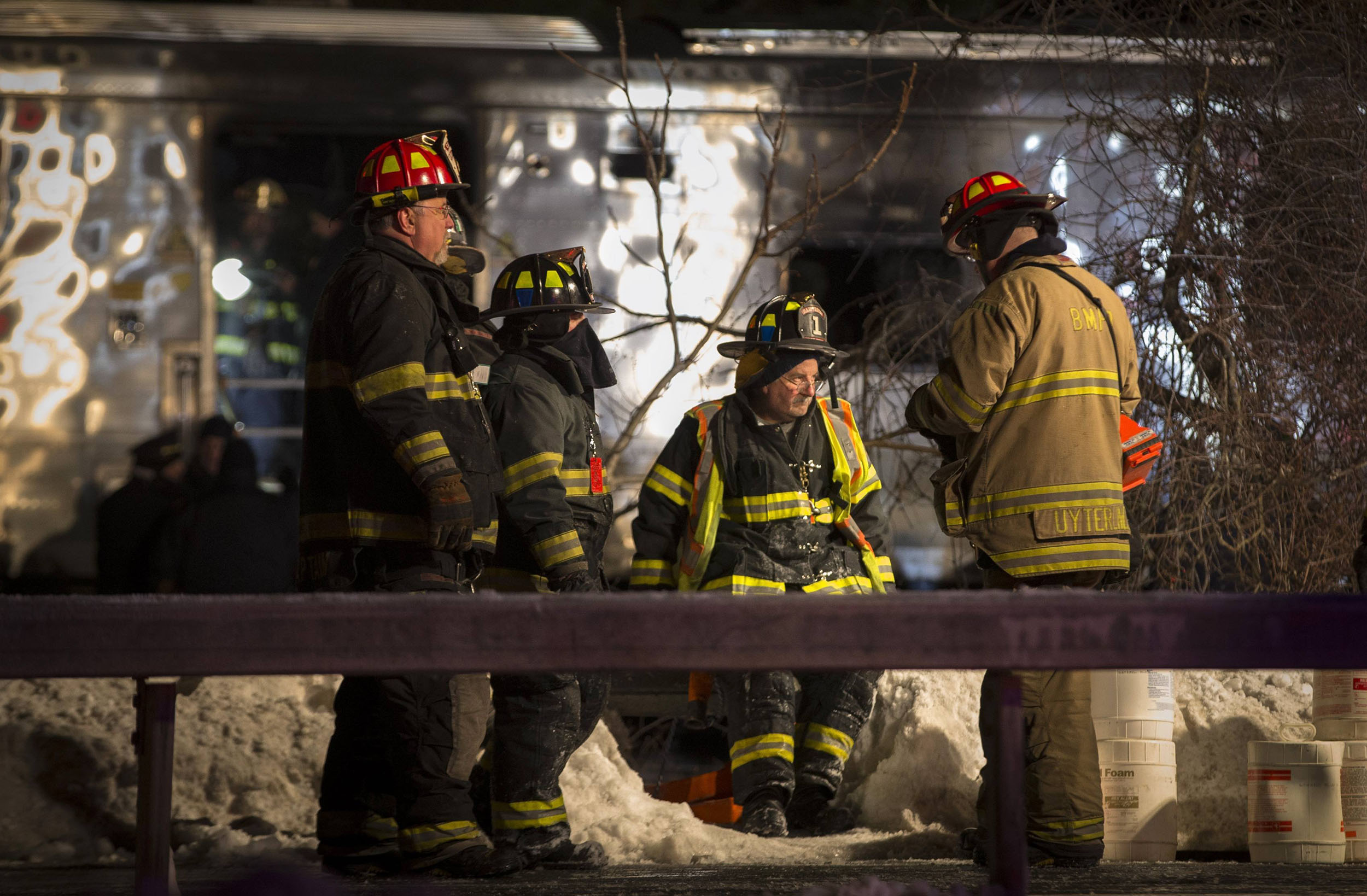Firefighters and Emergency workers stand near a burnt Metropolitan Transportation Authority Metro North Railroad commuter train car near the town of Valhalla
