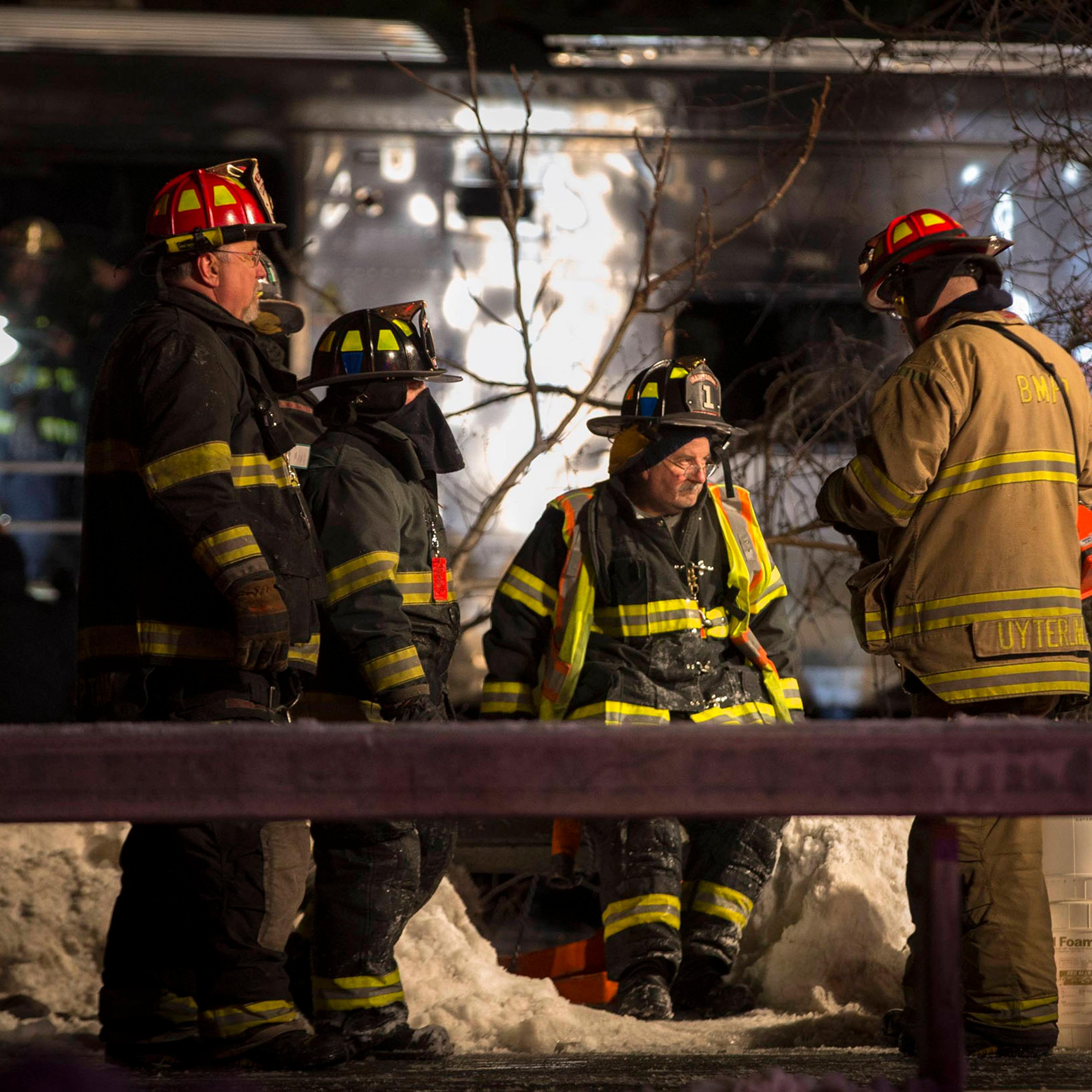 Firefighters and Emergency workers stand near a burnt Metropolitan Transportation Authority Metro North Railroad commuter train car near the town of Valhalla