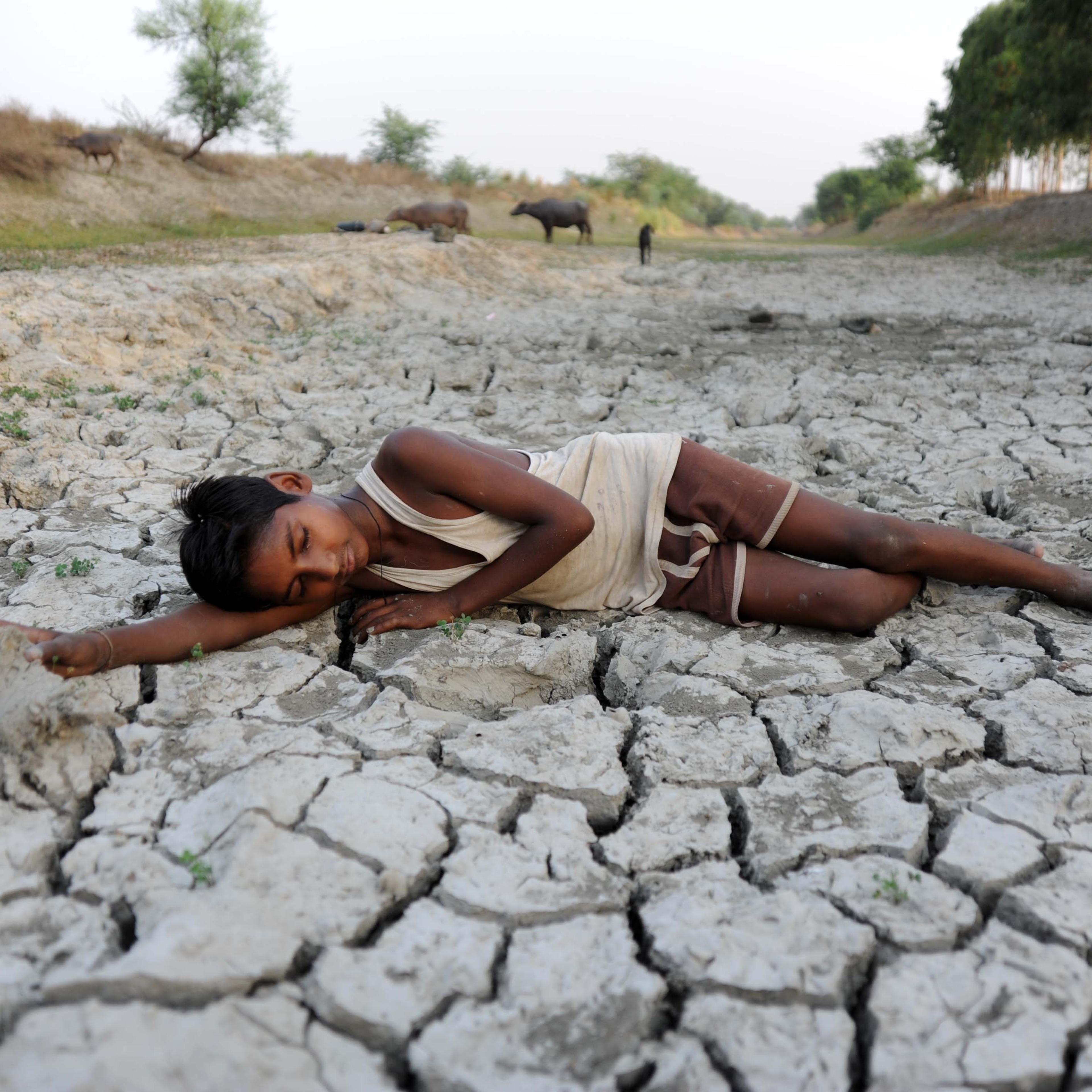 A child lies down on a dry bed of parched mud that is the