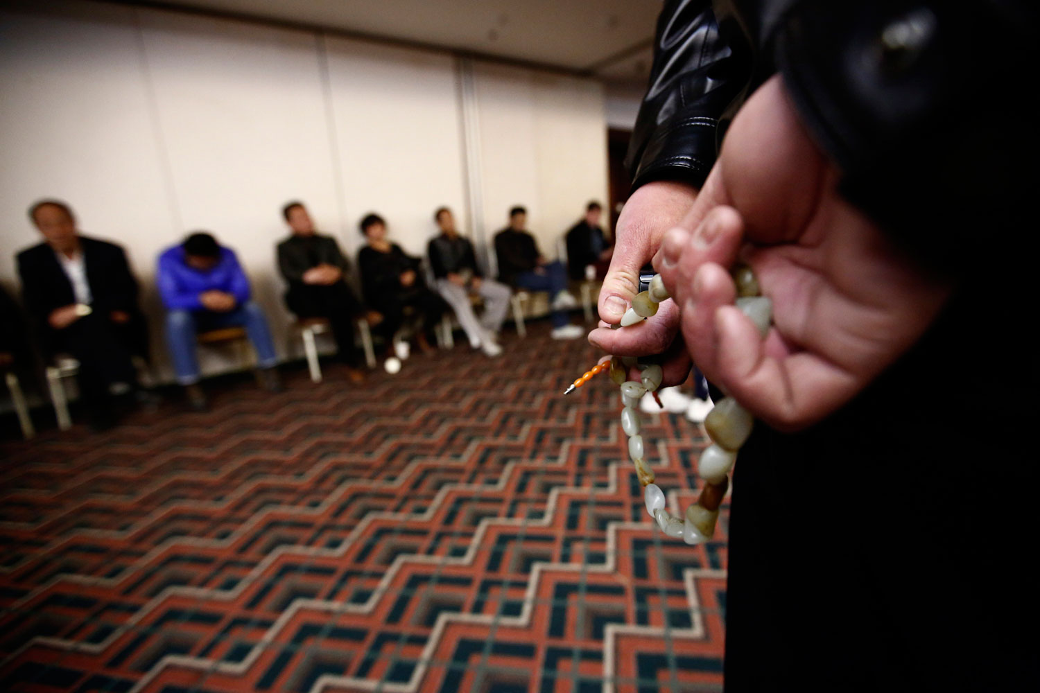 A family member of a passenger onboard the missing Malaysia Airlines flight MH370 fingers prayer beads as he listens to a briefing from the airline company with other family members (in background) at a hotel in Beijing, March 18, 2014.