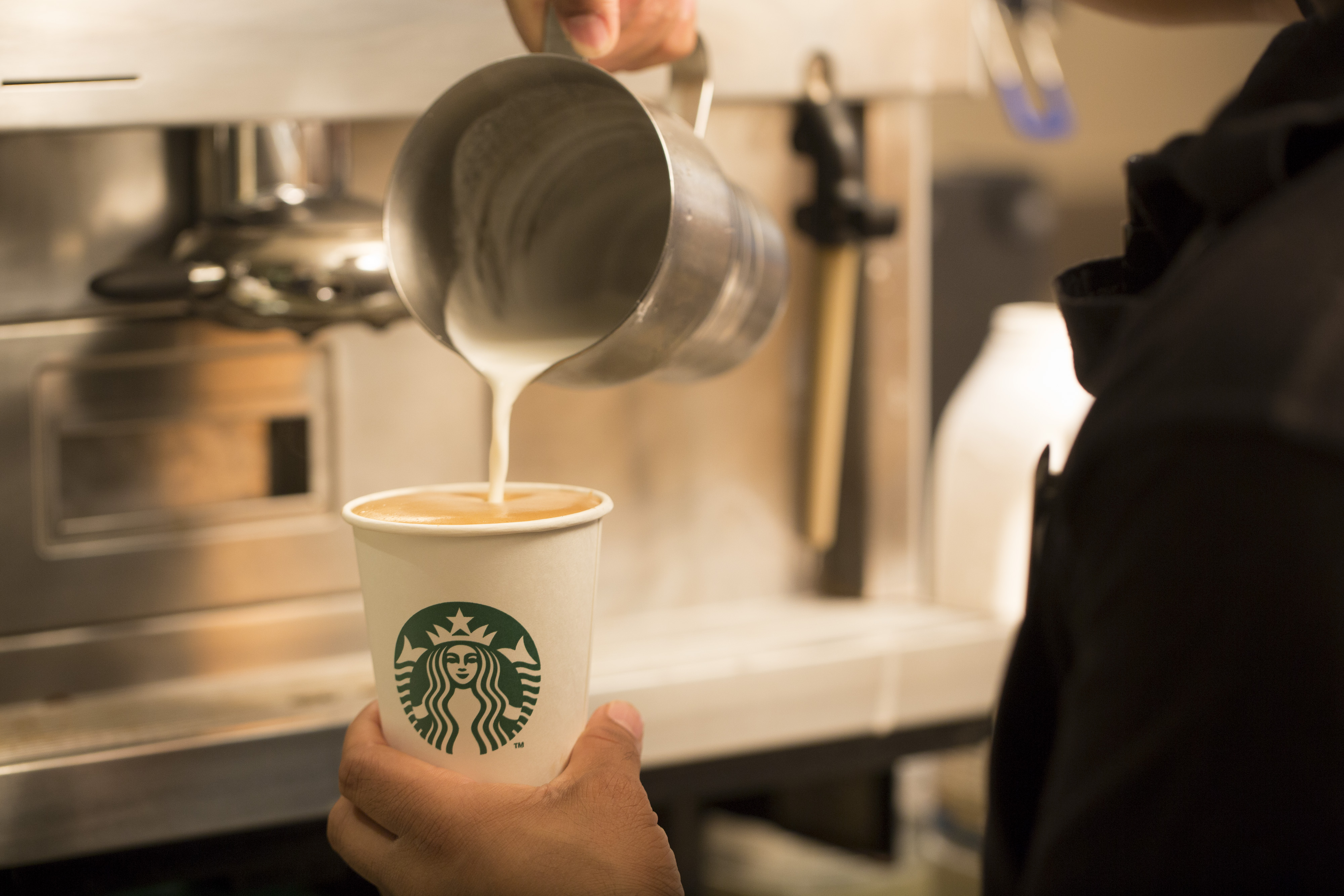 An employee pours milk into a cardboard coffee cup inside a Starbucks Corp. coffee shop in London, U.K., on Monday, Jun. 9, 2014.