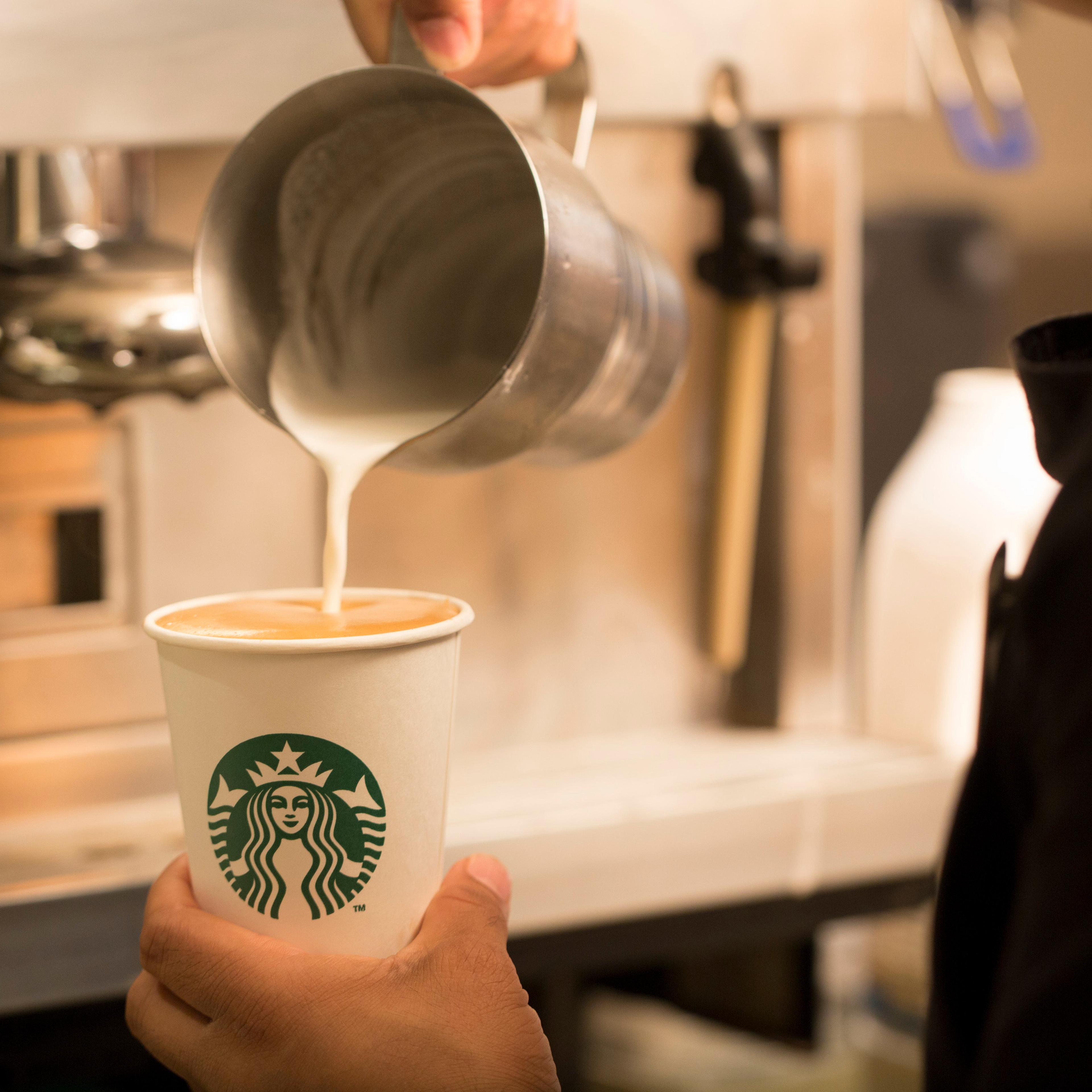 An employee pours milk into a cardboard coffee cup inside a Starbucks Corp. coffee shop in London, U.K., on Monday, Jun. 9, 2014.