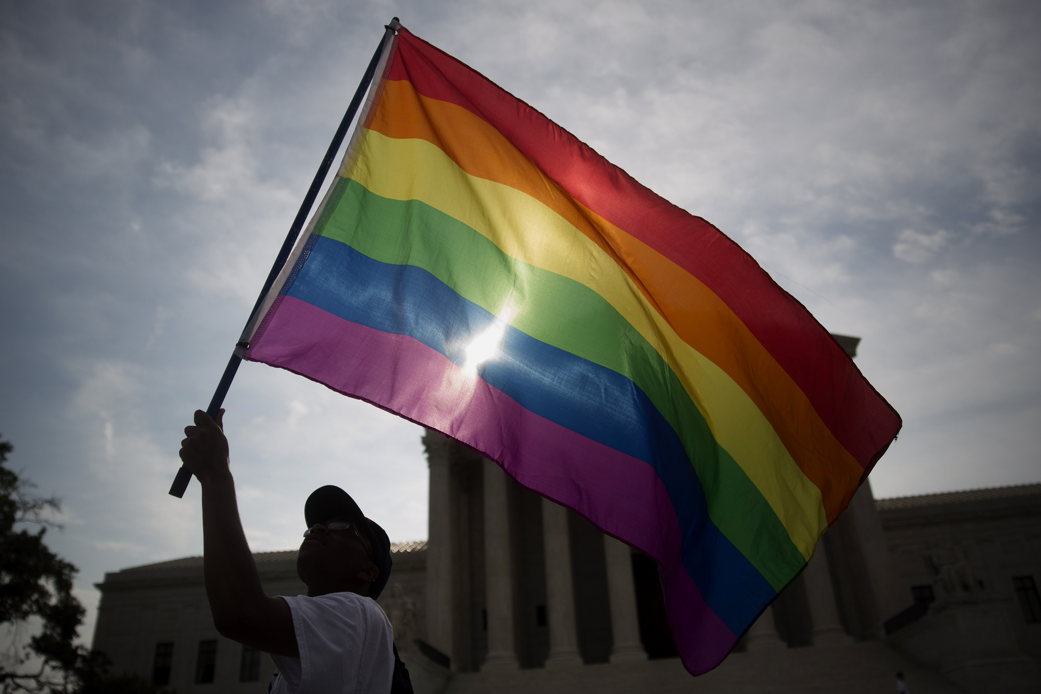 Carlos McKnight, from Washington, D.C., waves a rainbow colored flag outside the U.S. Supreme Court in Washington, D.C., U.S., on Friday, June 26, 2015. The high court will decide by the end of the month whether the Constitution gives gays the right to m