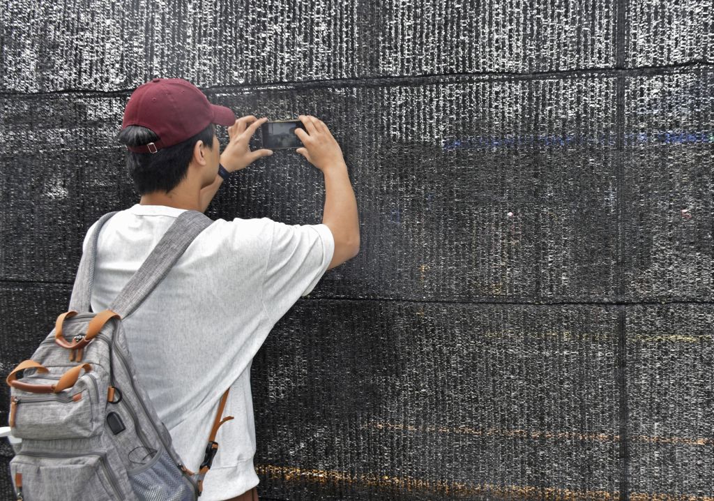 A man takes a picture through a hole made in a large black screen that was set up to block the view of Mount Fuji in the town of Fujikawaguchiko, Yamanashi Prefecture, on May 24, 2024.