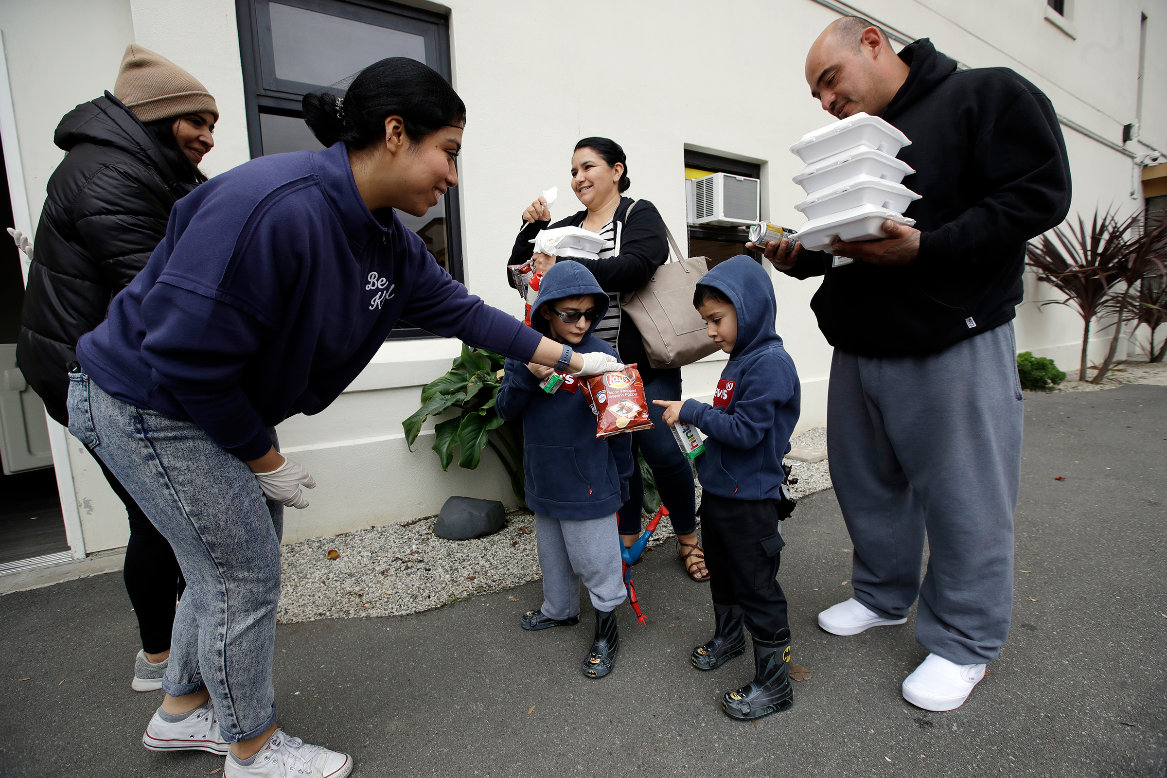 Volunteer Pahola Campos, second from left, hands out lunches to the Garcia family — mom Marie, dad Sergio, at right, and their children — on Mar. 16 at a food distribution center set up by the Dream Center for those in need due to the coronavirus outbreak in Los Angeles 
