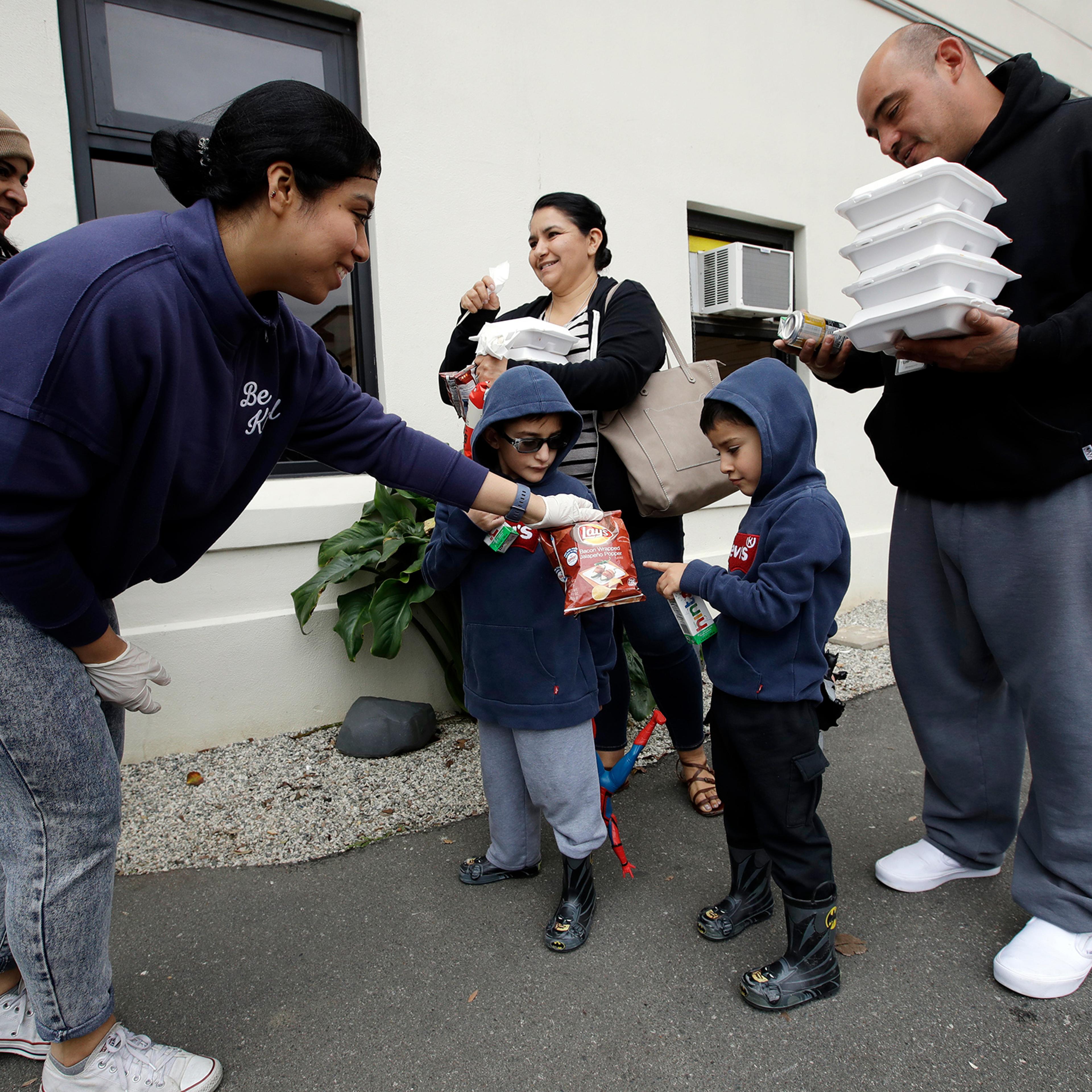 Volunteer Pahola Campos, second from left, hands out lunches to the Garcia family — mom Marie, dad Sergio, at right, and their children — on Mar. 16 at a food distribution center set up by the Dream Center for those in need due to the coronavirus outbreak in Los Angeles