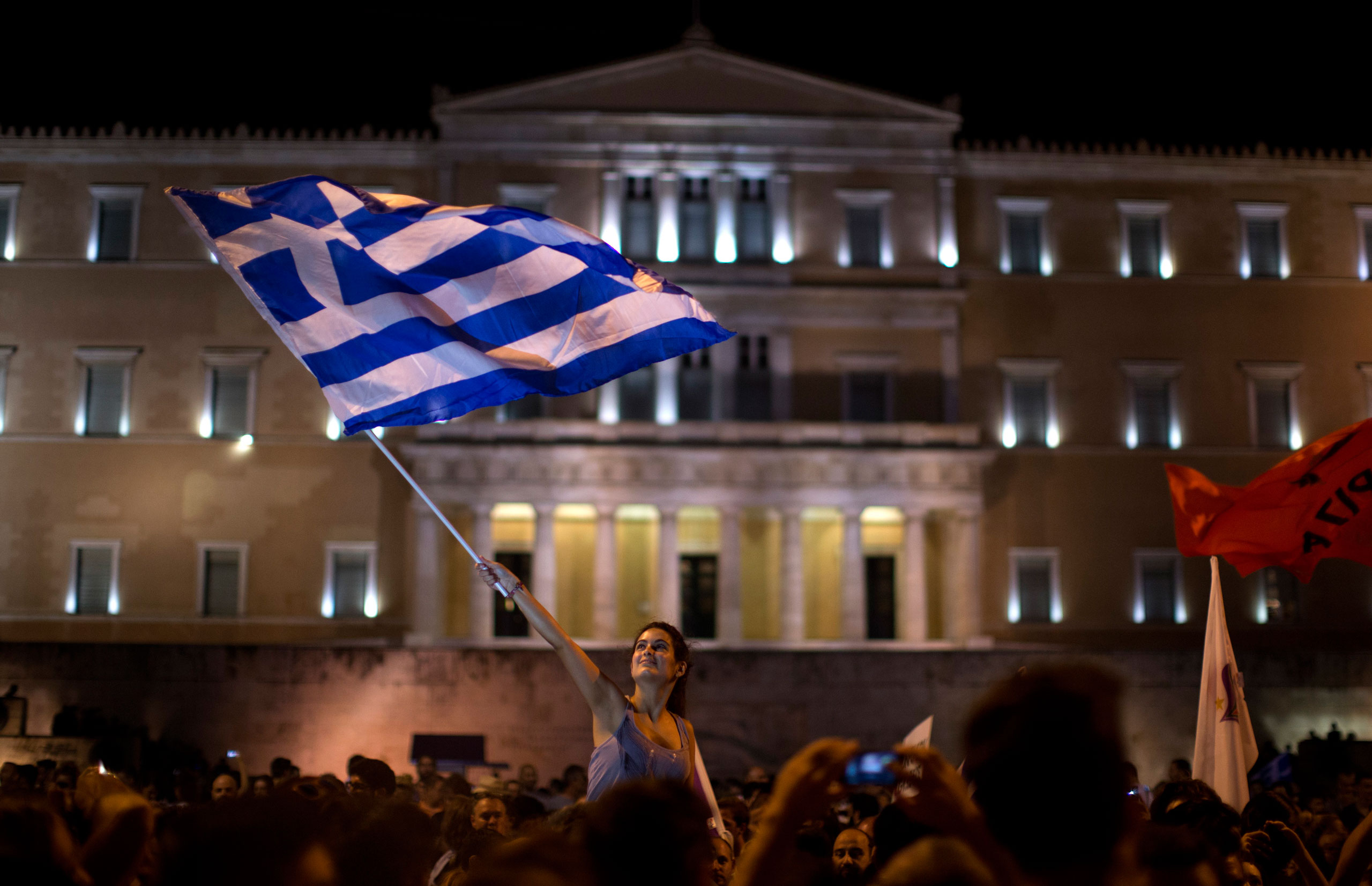 A supporter of the No vote waves a Greek flag in front of the parliament after the results of the referendum at Syntagma square in Athens, Sunday, July 5, 2015. Greeks overwhelmingly rejected creditors' demands for more austerity in return for rescue loa