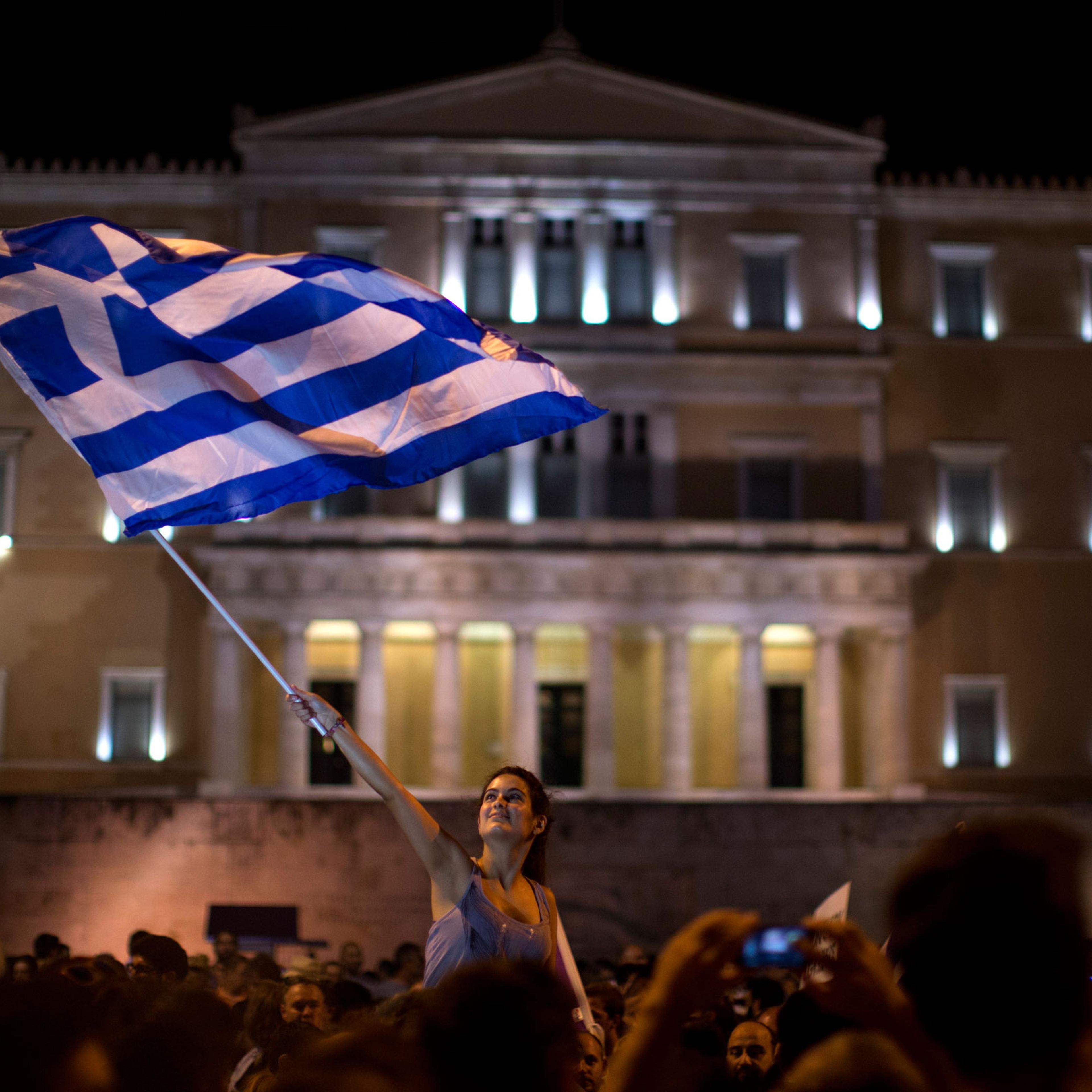 A supporter of the No vote waves a Greek flag in front of the parliament after the results of the referendum at Syntagma square in Athens, Sunday, July 5, 2015. Greeks overwhelmingly rejected creditors' demands for more austerity in return for rescue loa