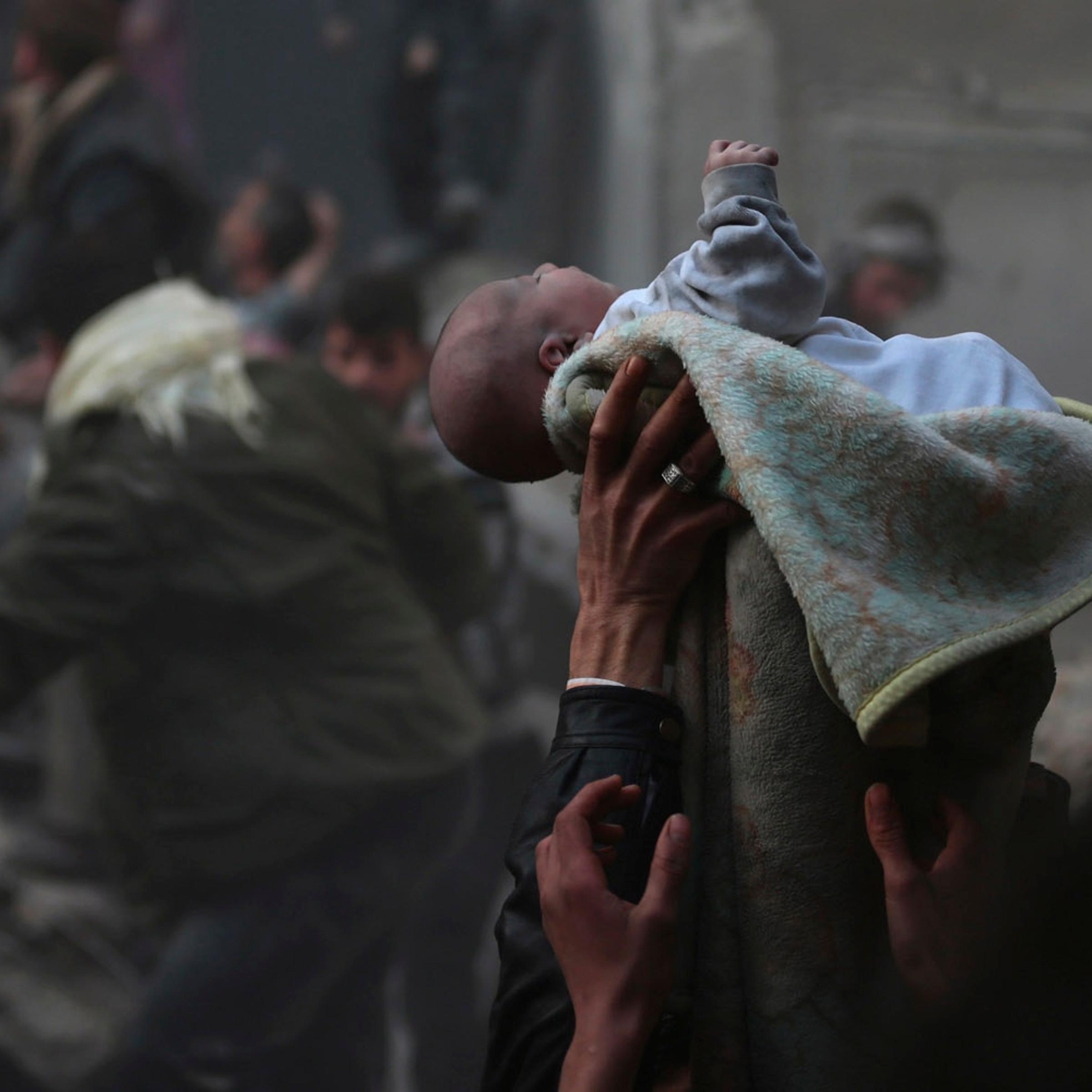 Men hold up a baby saved from under rubble, who survived an airstrike in the Duma neighbourhood of Damascus