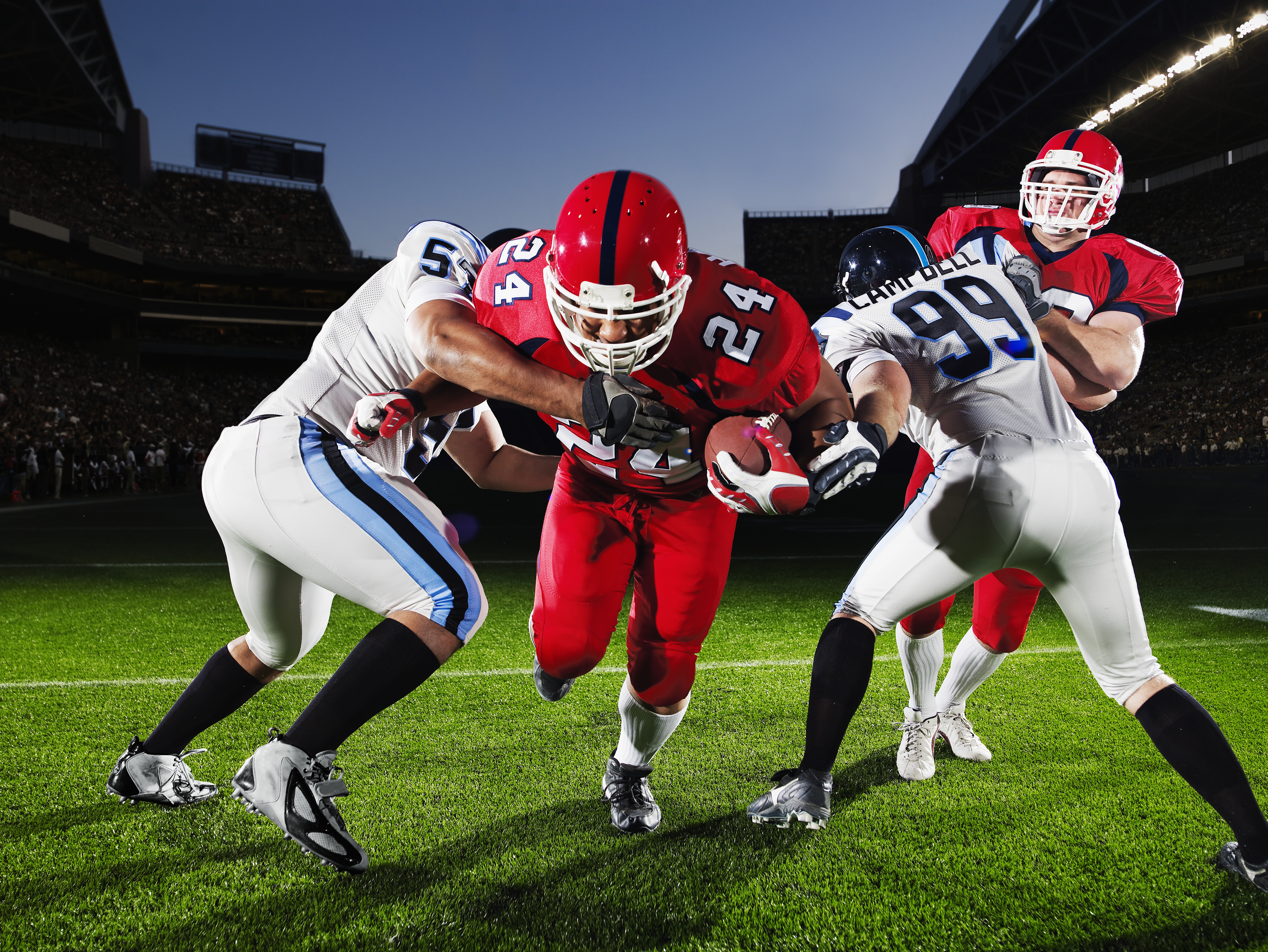 Professional football running back running through defenders crowded stadium in background