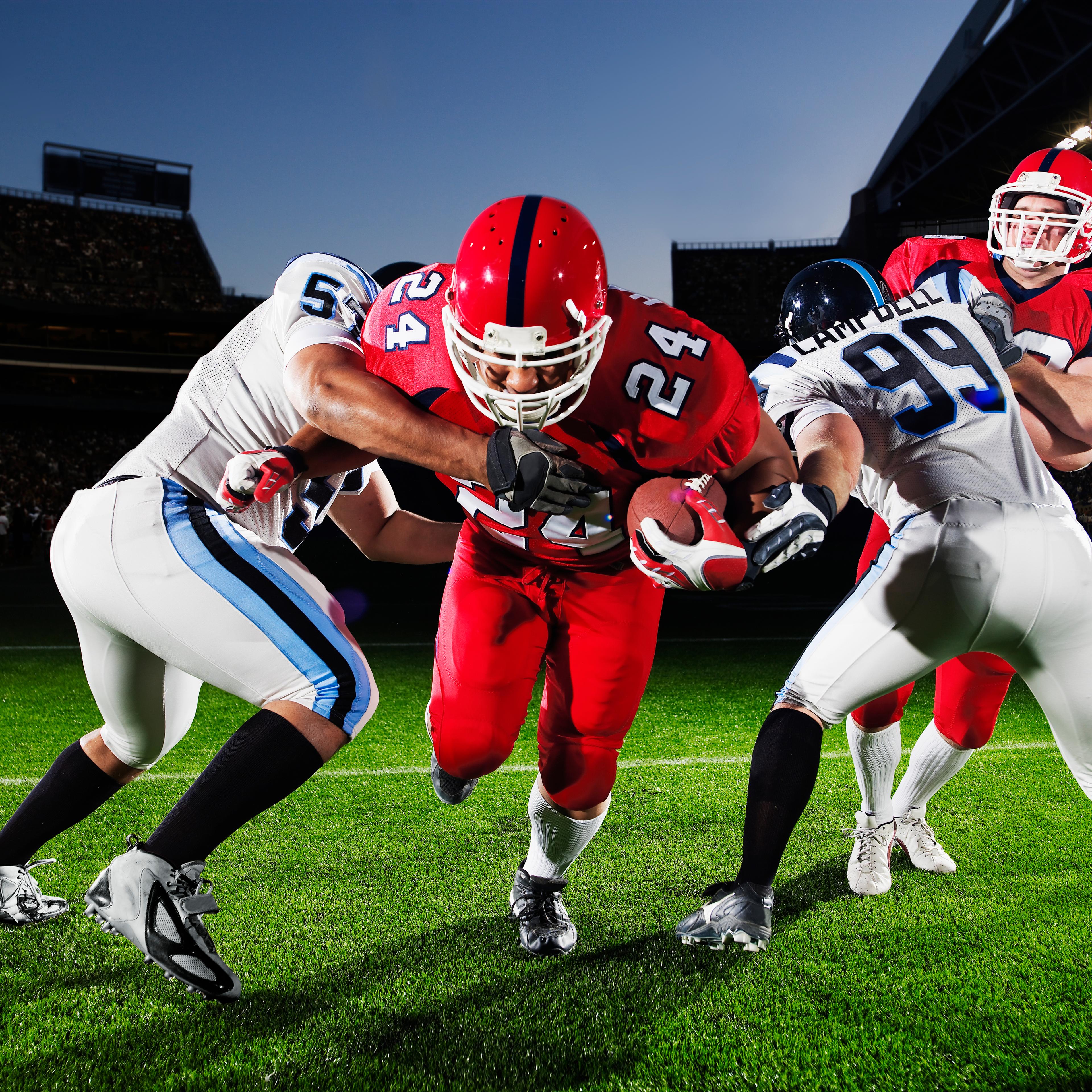 Professional football running back running through defenders crowded stadium in background