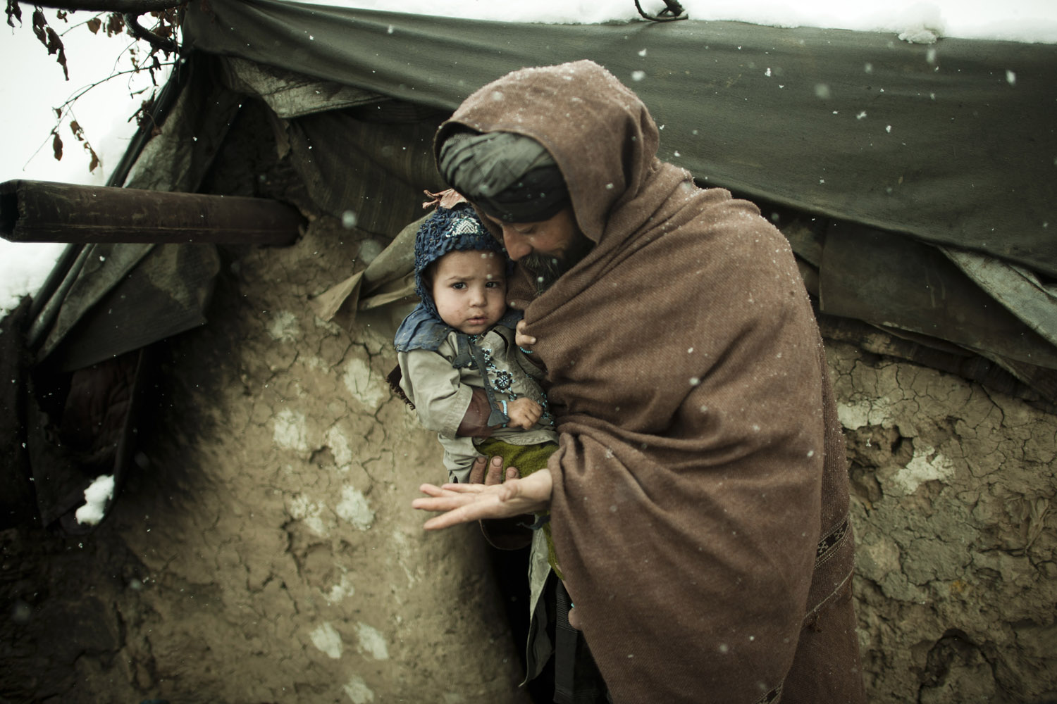 Ibrahim holds his youngest son outside a mud hut where he lives with his wife and 11 children. The same camp buried at least two children who died due to the freezing temperatures in late January, 2012.