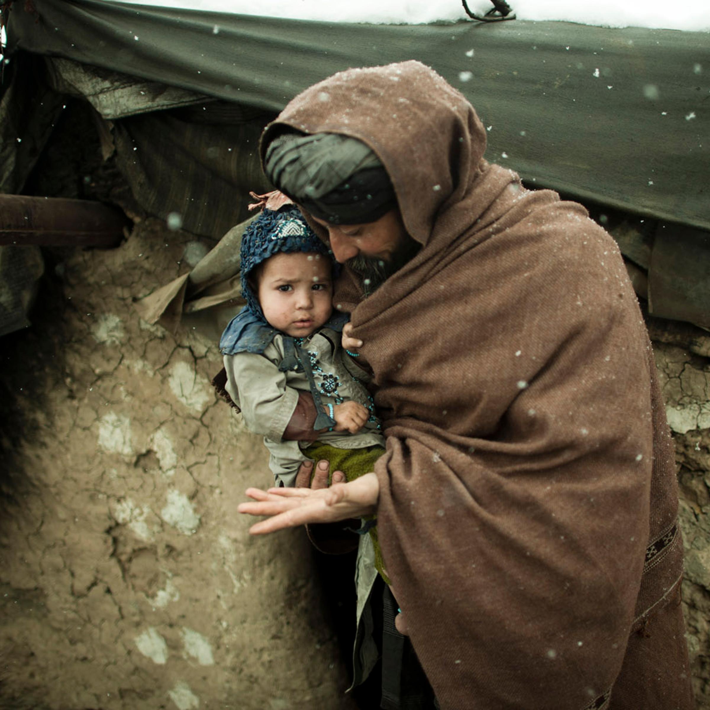 Ibrahim holds his youngest son outside a mud hut where he lives with his wife and 11 children. The same camp buried at least two children who died due to the freezing temperatures in late January, 2012.