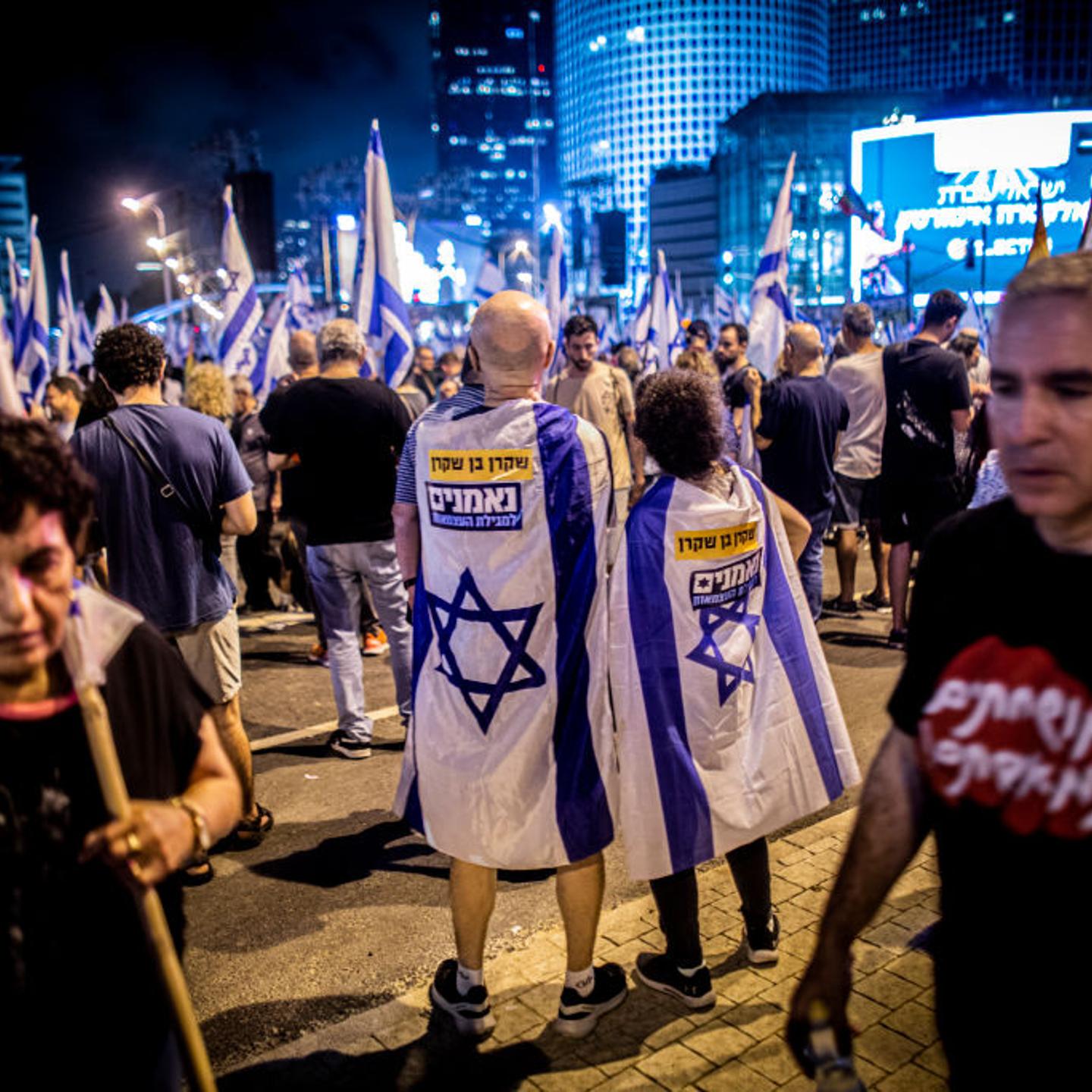Protestors draped in the Israeli flags stand together during