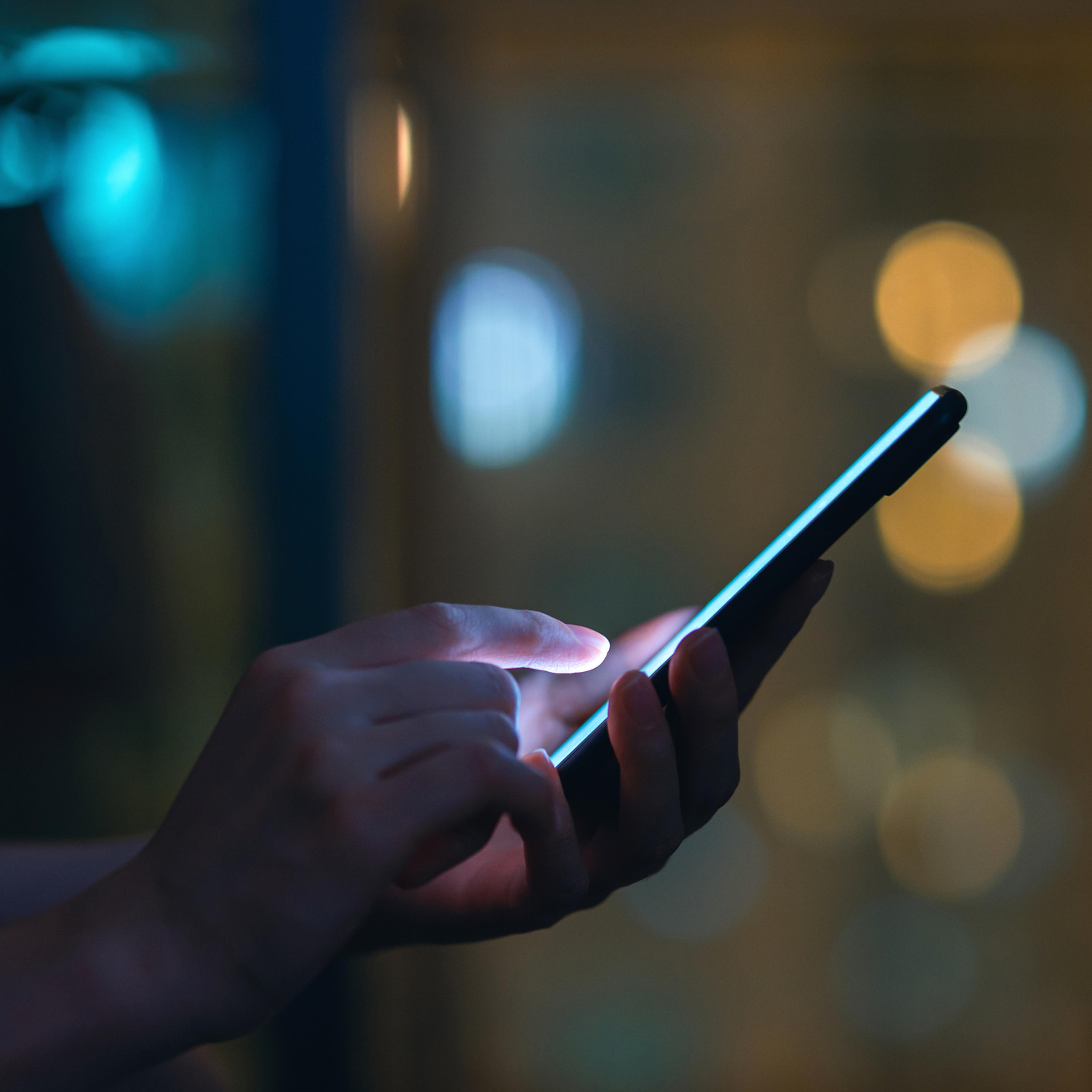 Close up of woman's hand using smartphone in the dark, against illuminated city light bokeh
