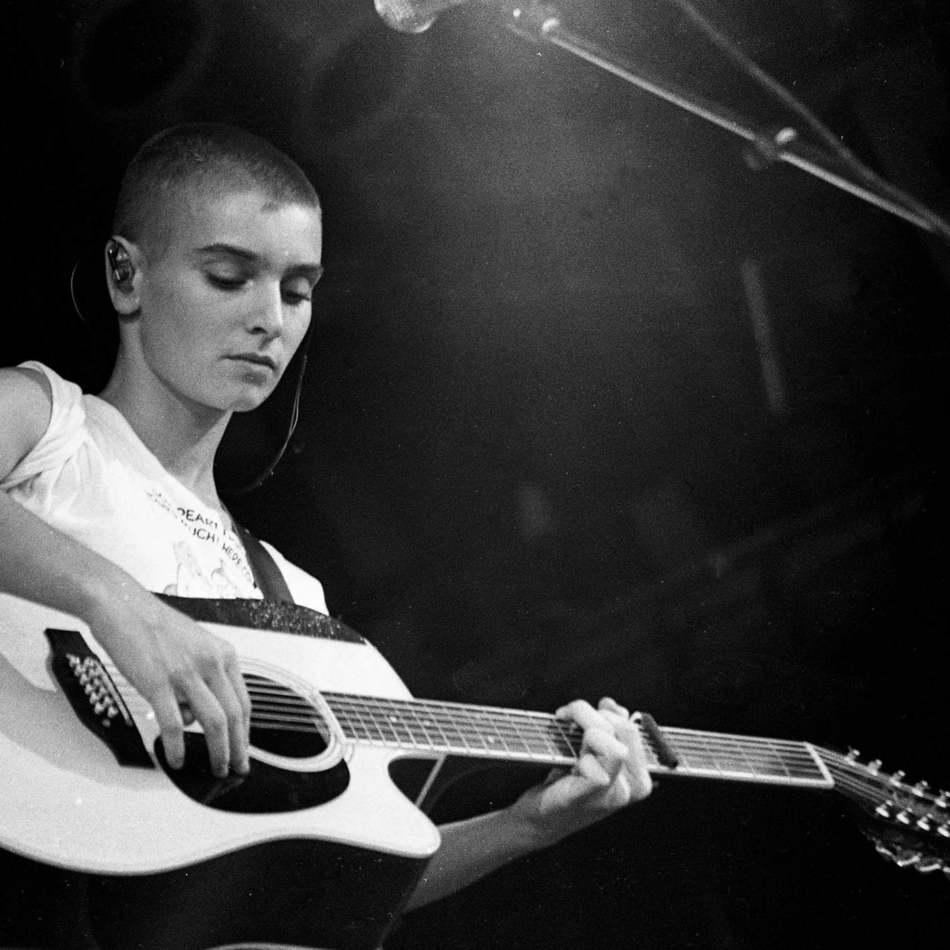 Sinead O'Connor plays the guitar on stage in a black and white photograph