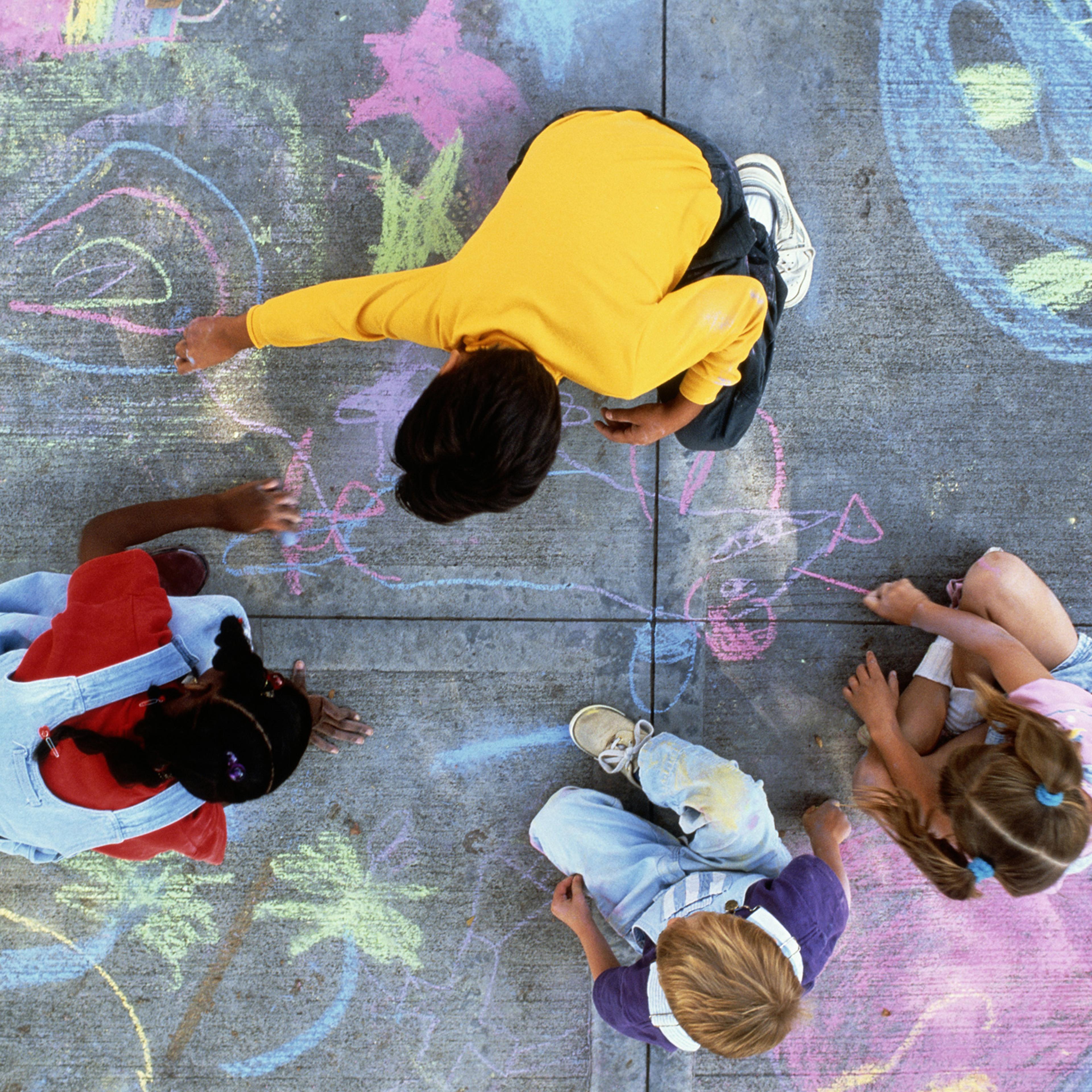 Four children drawing with chalk on pavement.