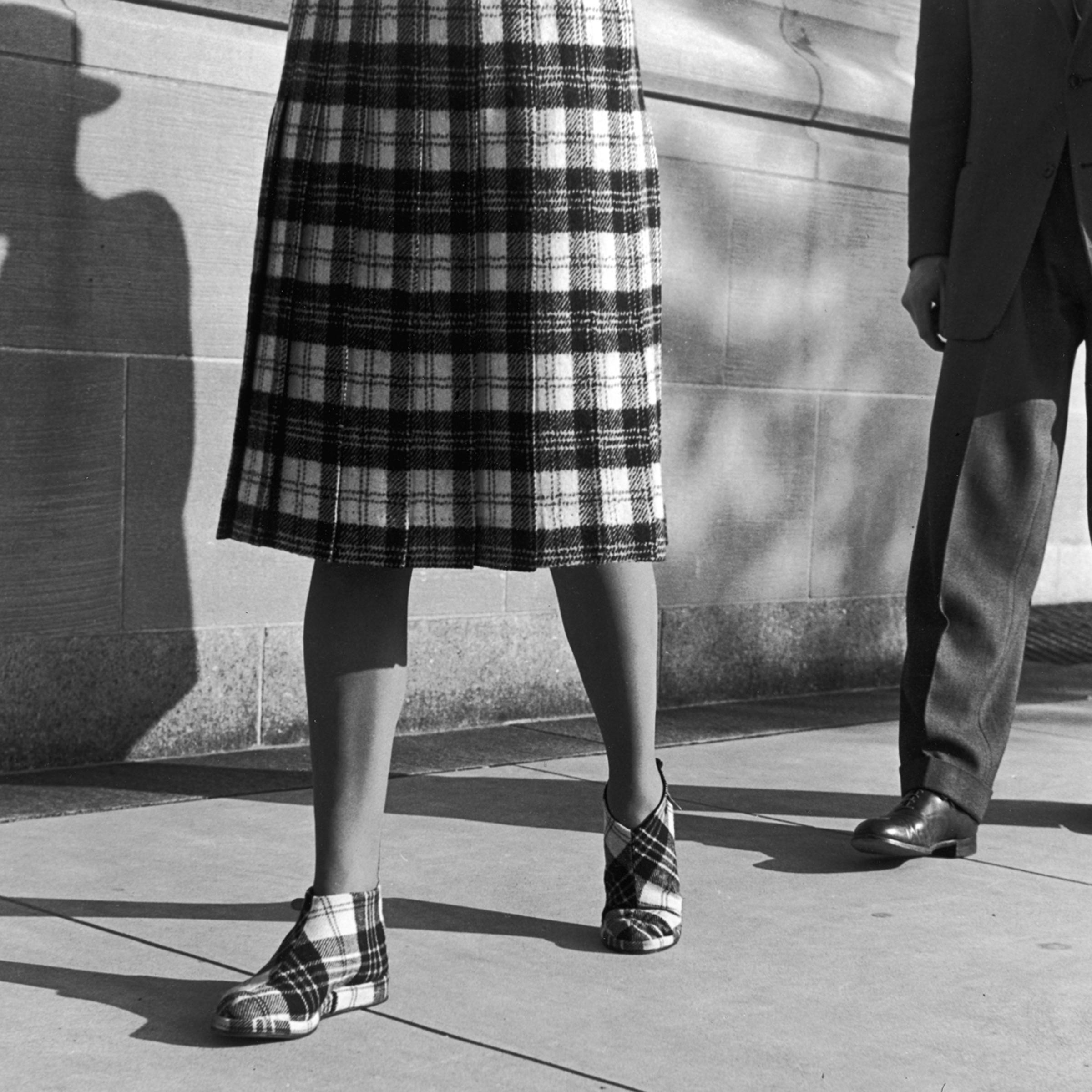 A woman in a plaid skirt and matching shoes, shadowed by a stranger, New York City, 1946.