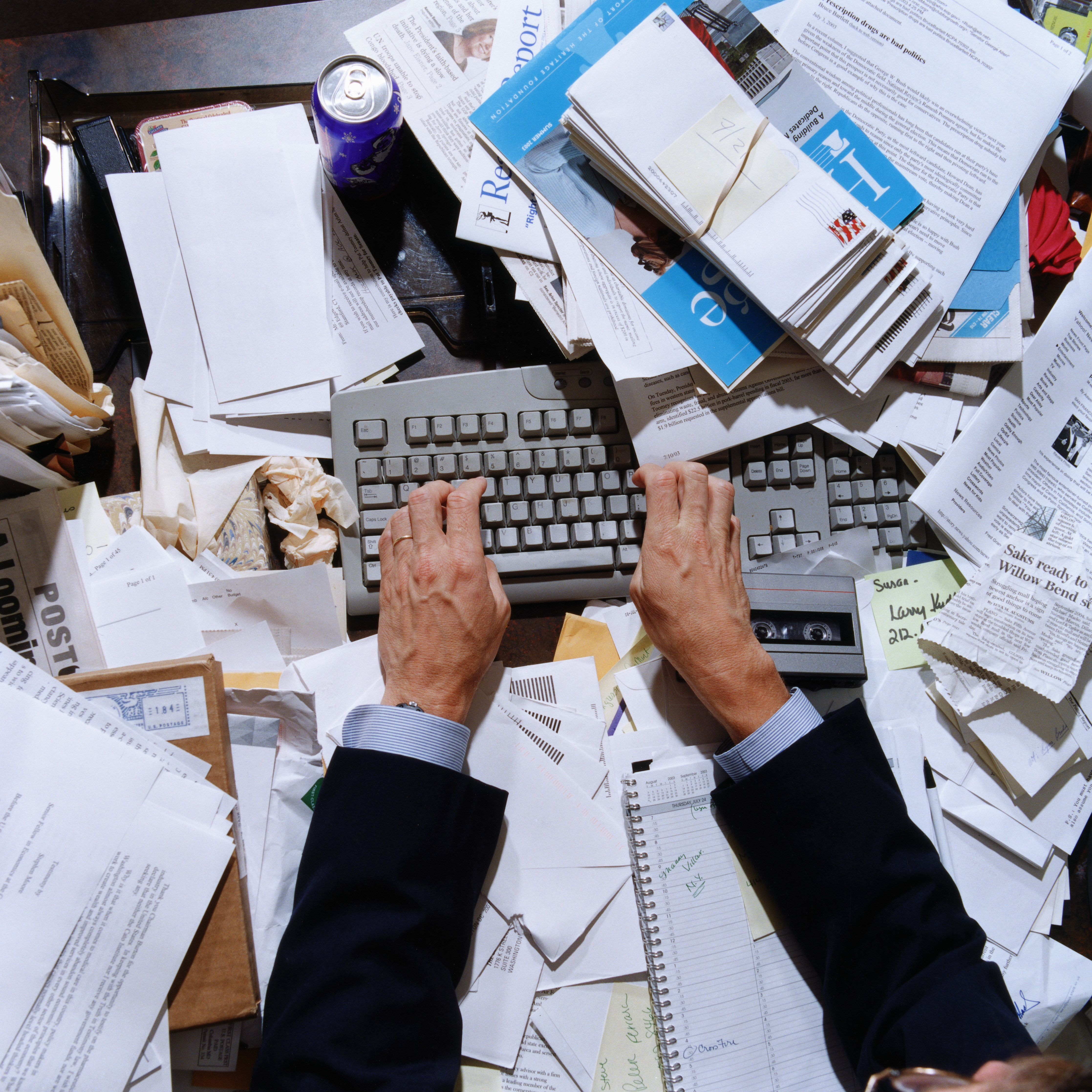 Male hands using computer keyboard with papers on desk, overhead view