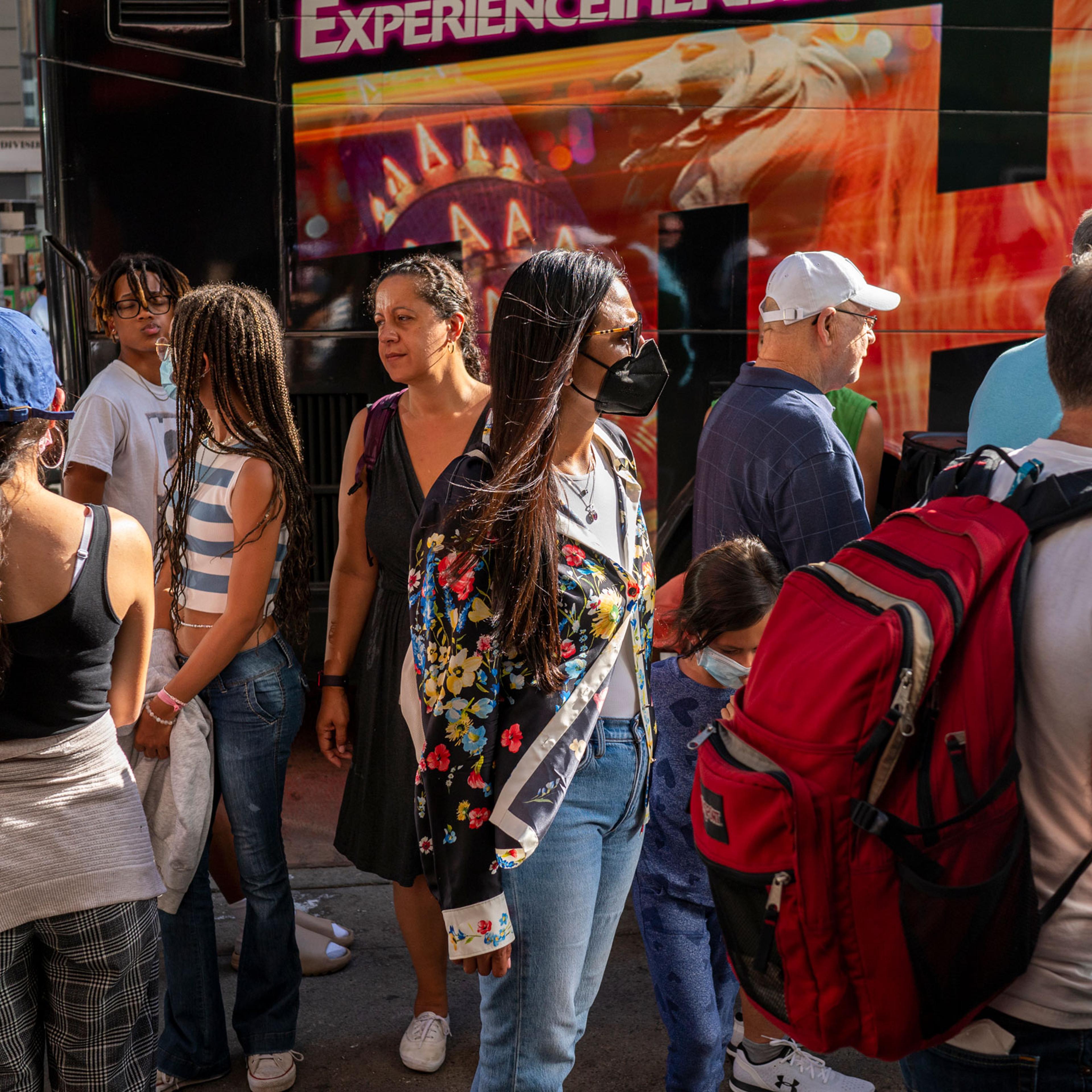 Tourists holding tickets for a bus tour stand in line