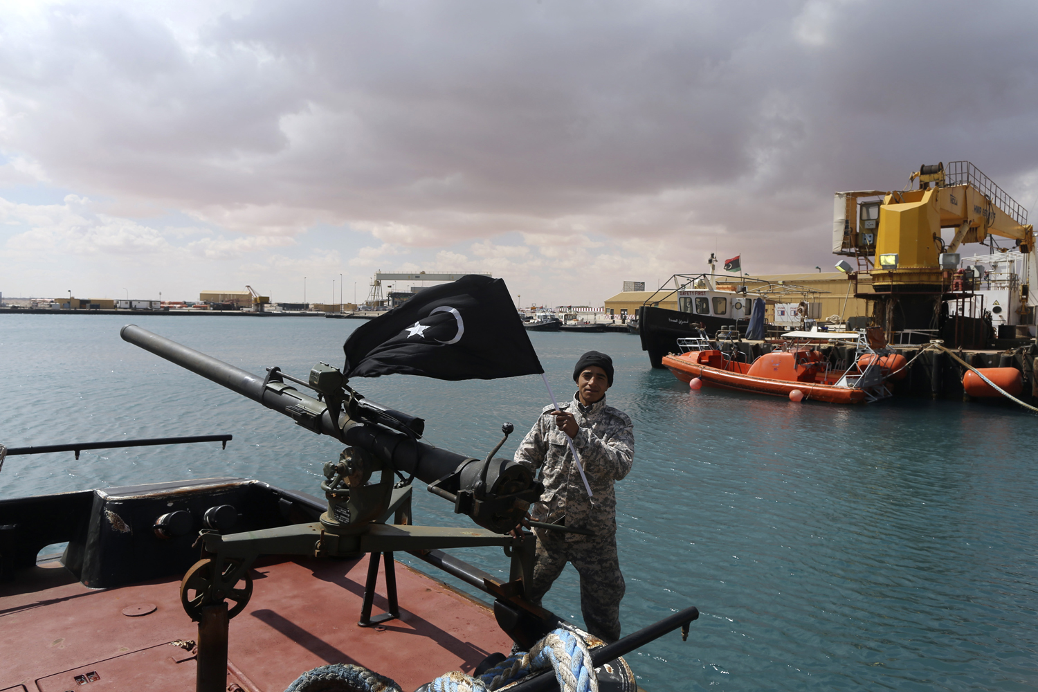 A rebel under Ibrahim Jathran holds the Cyrenaica flag while standing on a boat at Es Sider port in Ras Lanuf