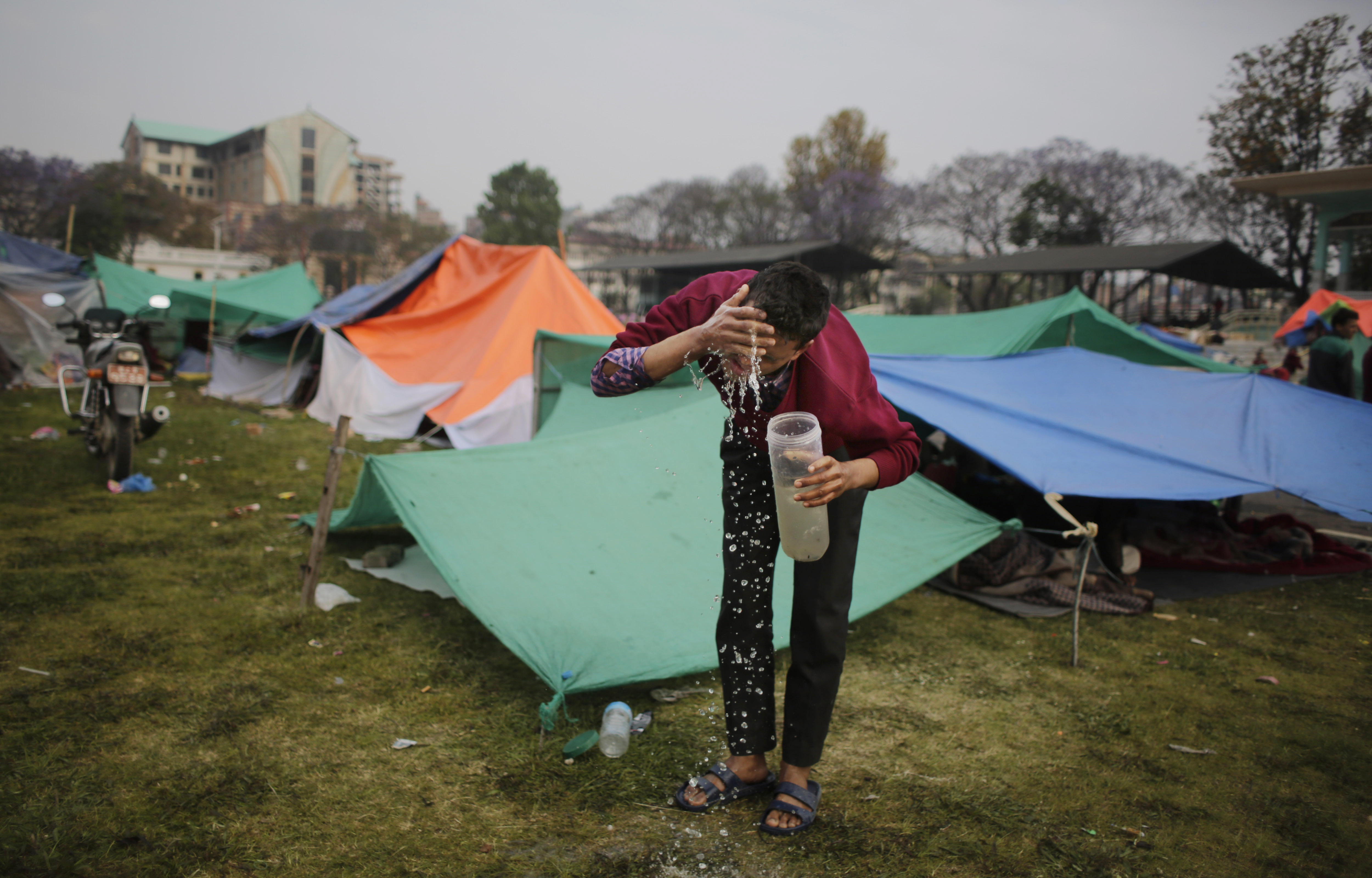 Survivor of Saturday's earthquake washes his face after spending night in an open ground from fears of earthquake tremors in Kathmandu, Nepal, Tuesday, April 28, 2015.