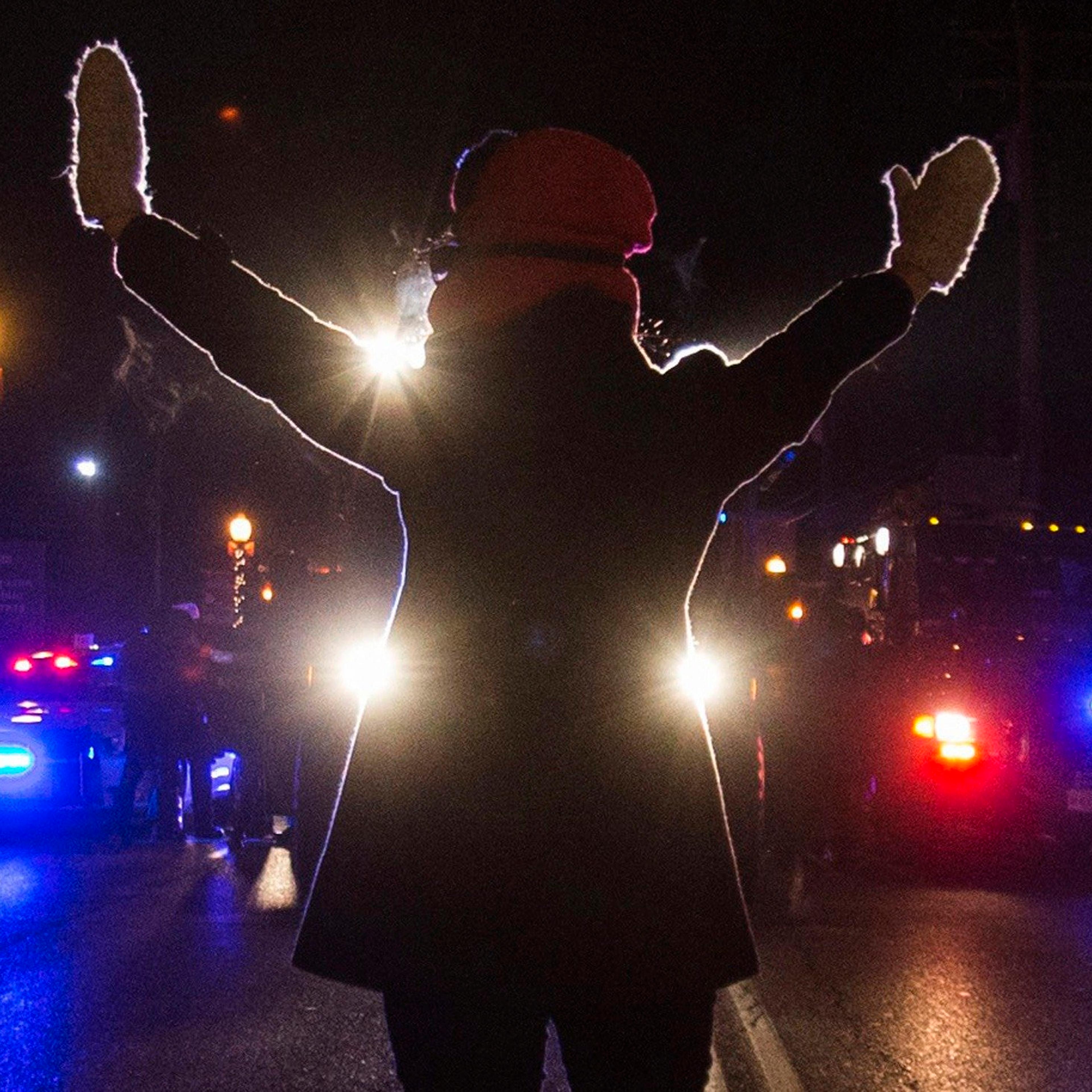 A female protester raises her hands while blocking police cars in Ferguson