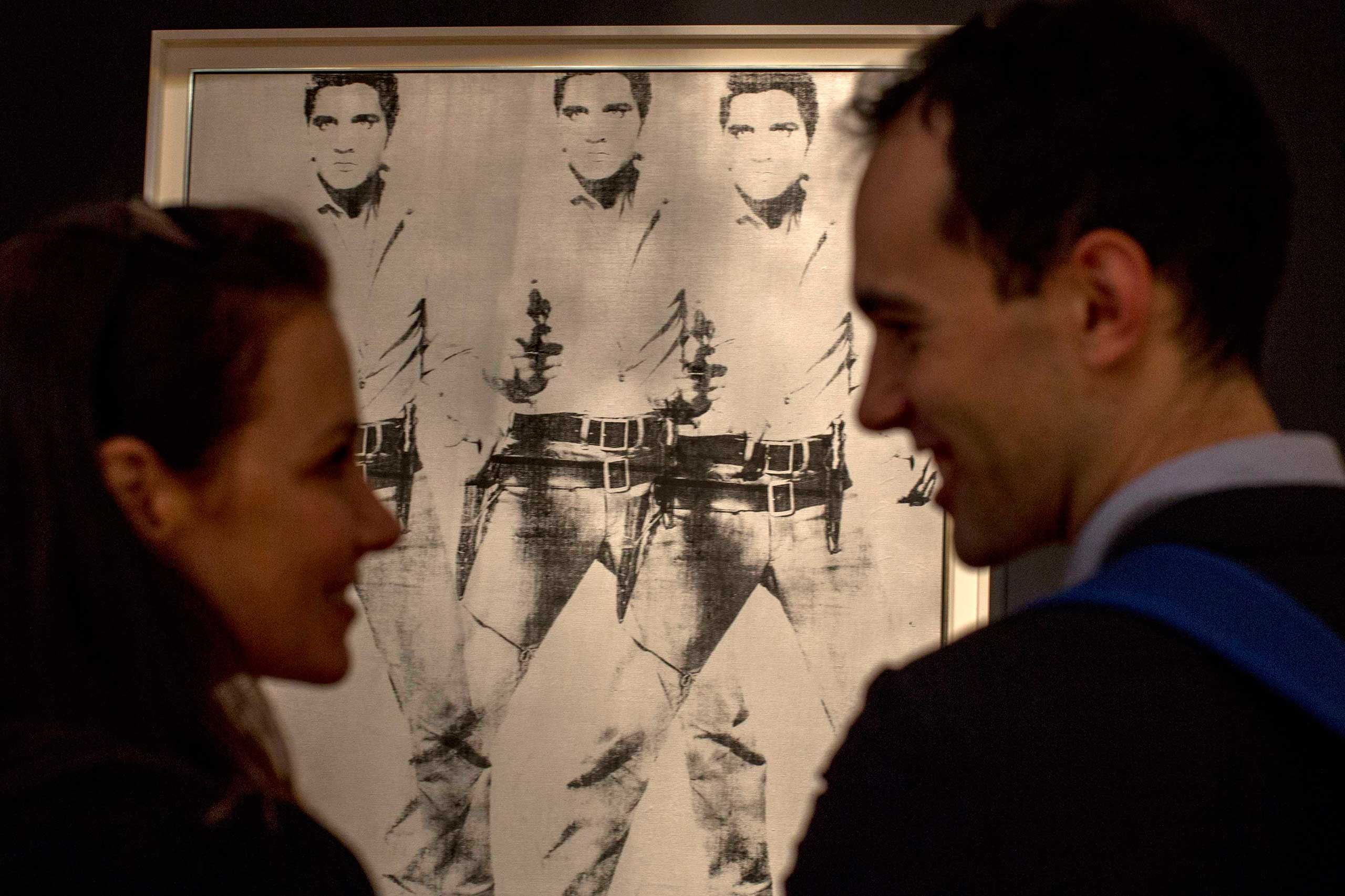 A couple talk in front of "Triple Elvis" by Andy Warhol during a media preview at Christie's auction house in New York, October 31, 2014.