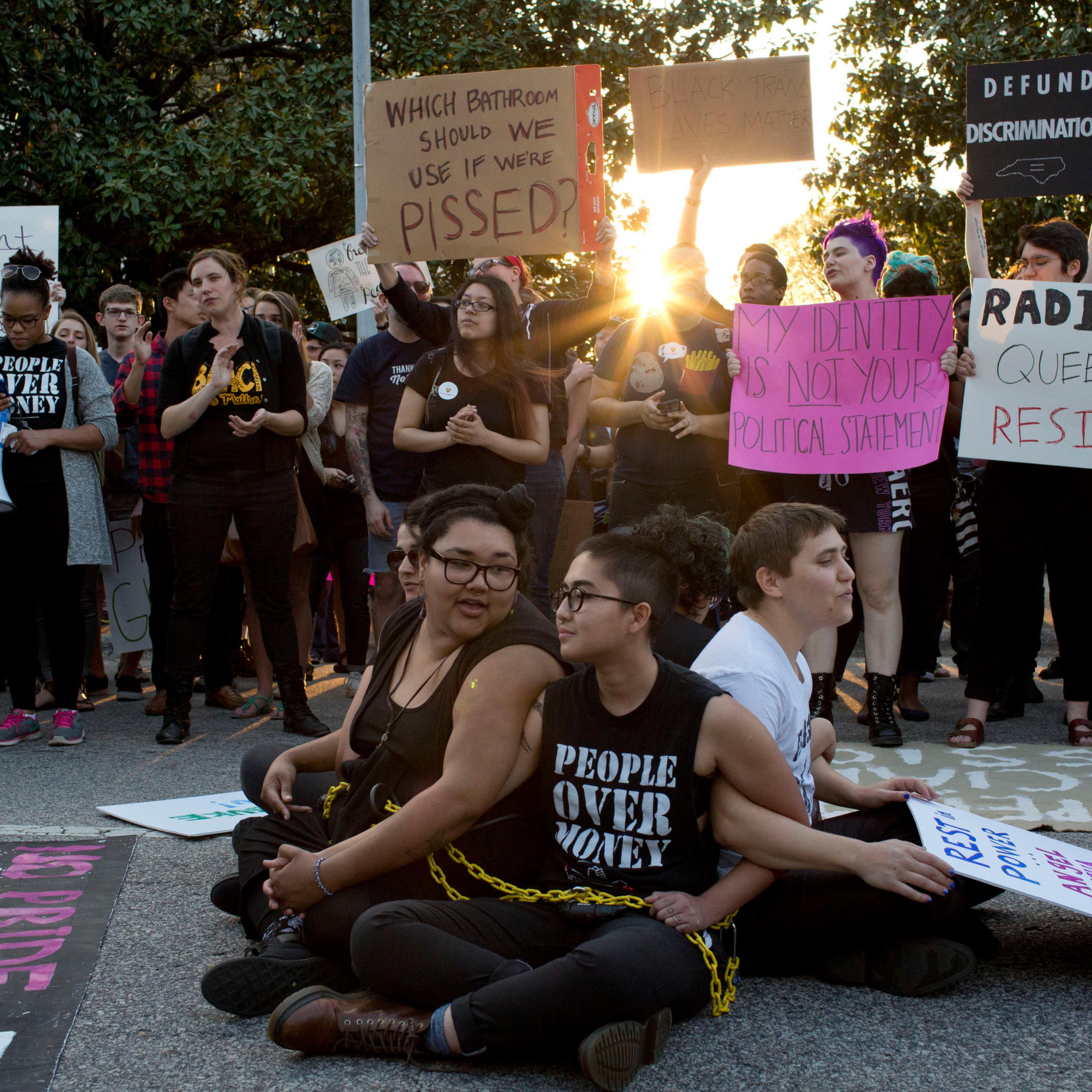 Front from left, demonstrators Jess Jude, Loan Tran and Noah Rubin-Blose, sit chained together in the middle of the street during a protest against House Bill 2 outside of the Governor's Mansion in Raleigh, N.C., on March 24, 2016,.