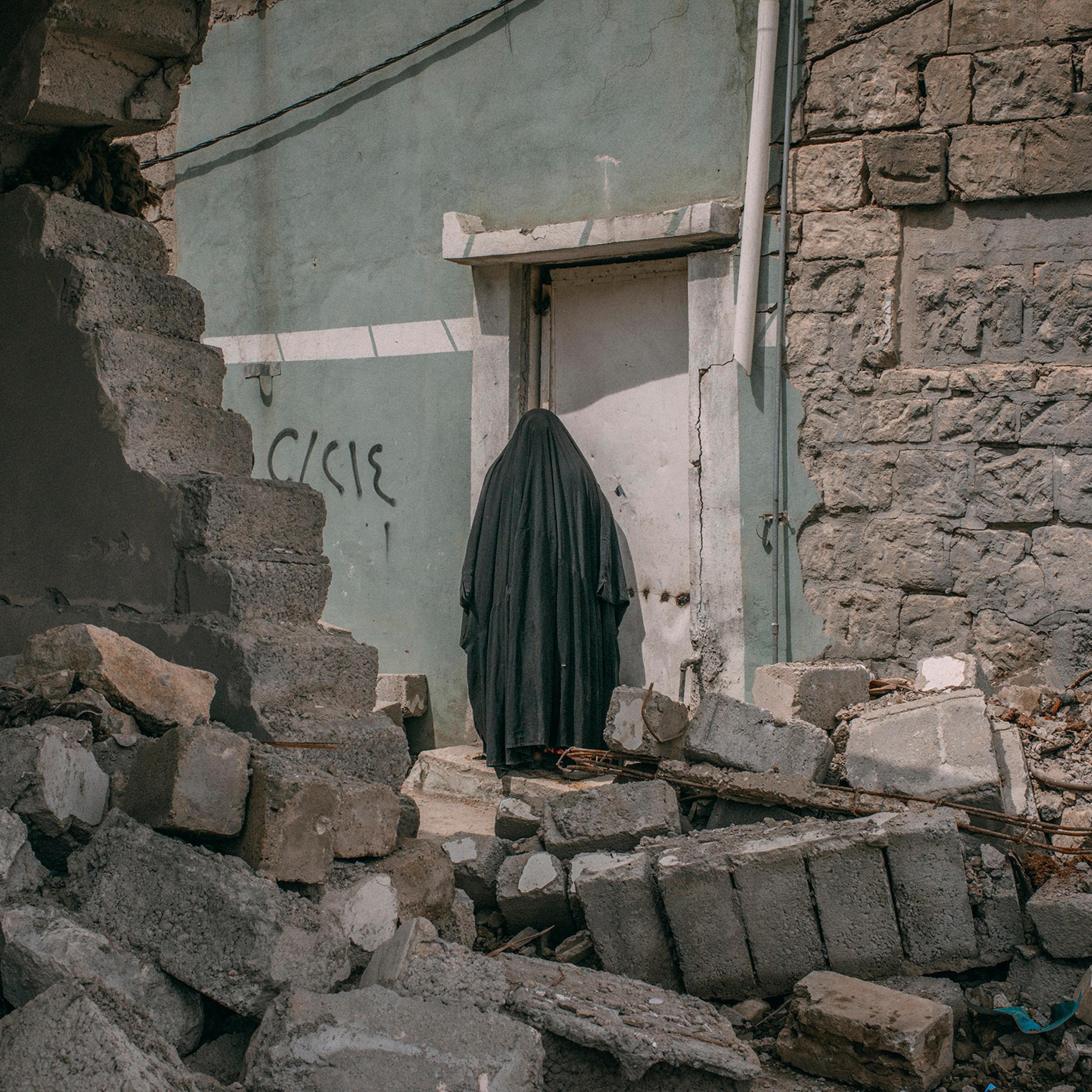 A woman stands among buildings damaged by airstrikes in southwest Mosul on April 3, 2017