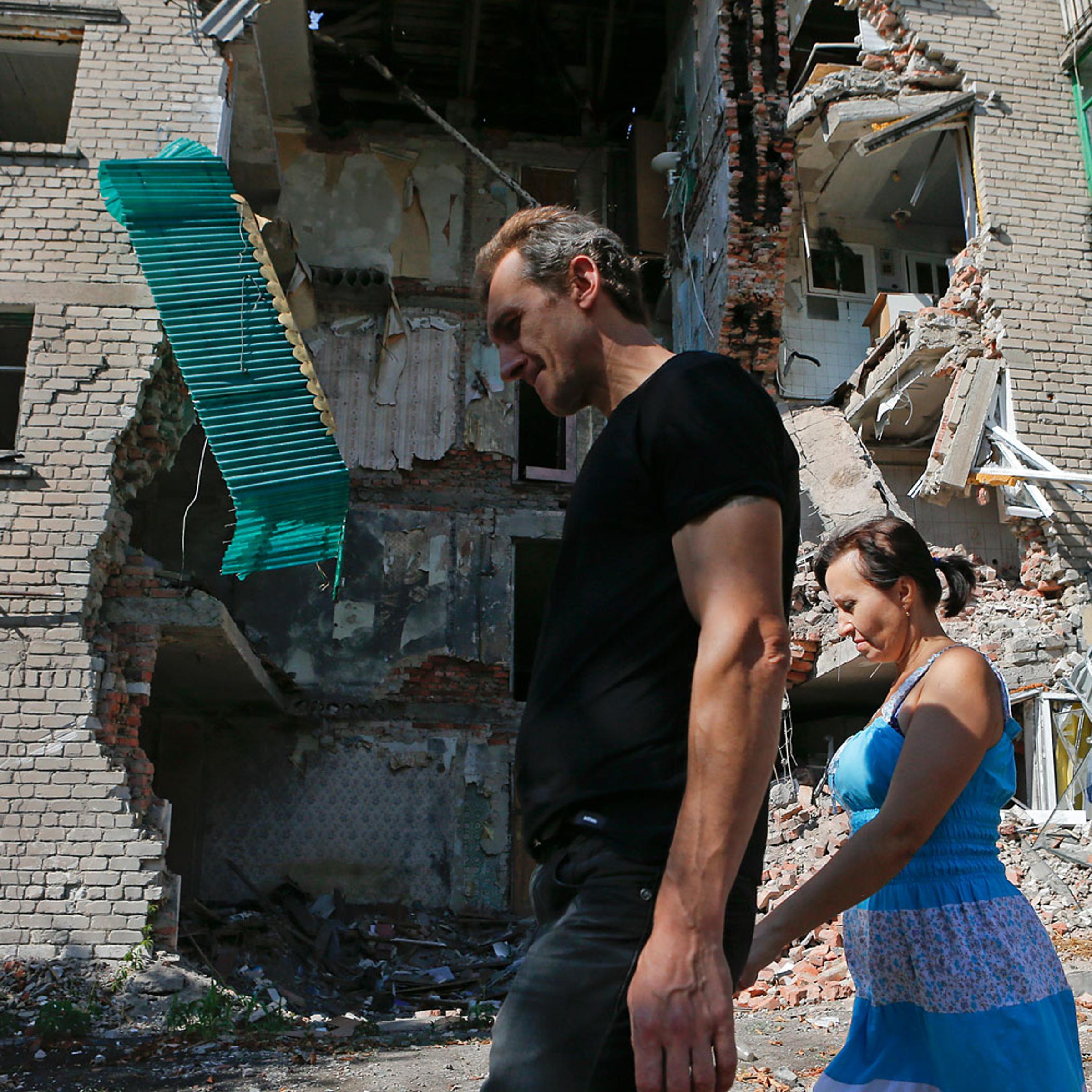 People walk past a building damaged by shelling in Snizhne (Snezhnoye), Donetsk region