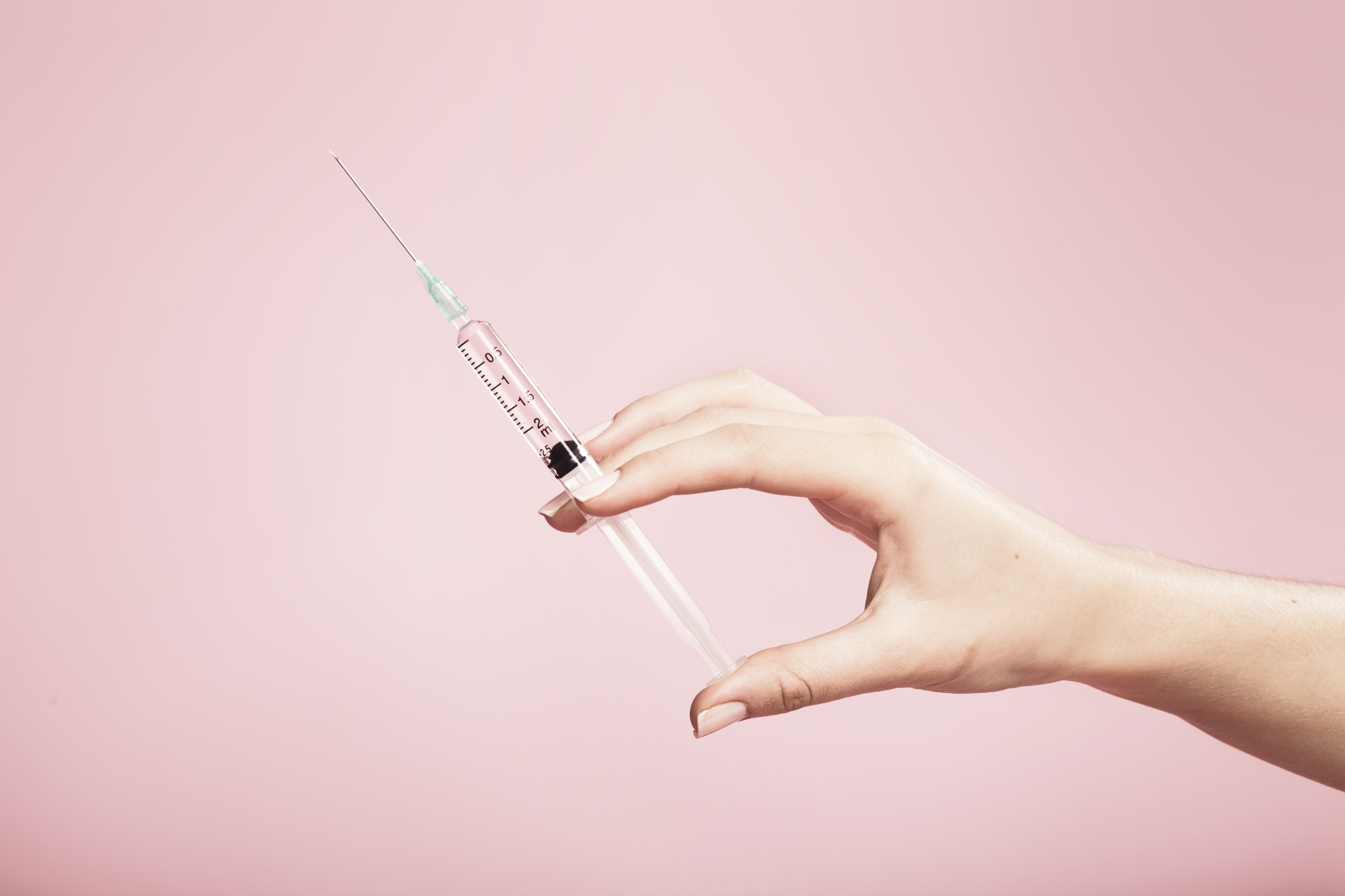 Hand holding syringe in plain pink background