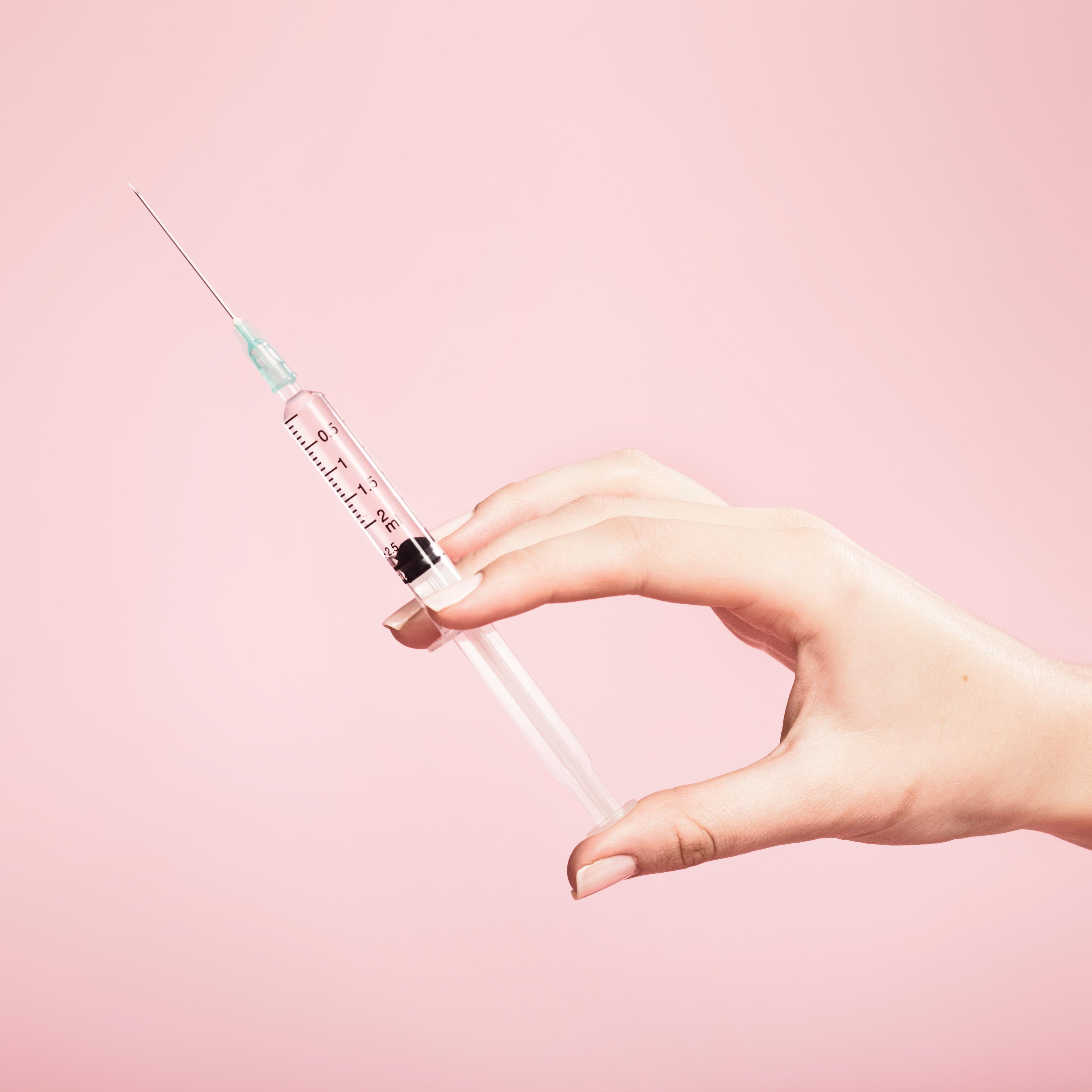 Hand holding syringe in plain pink background