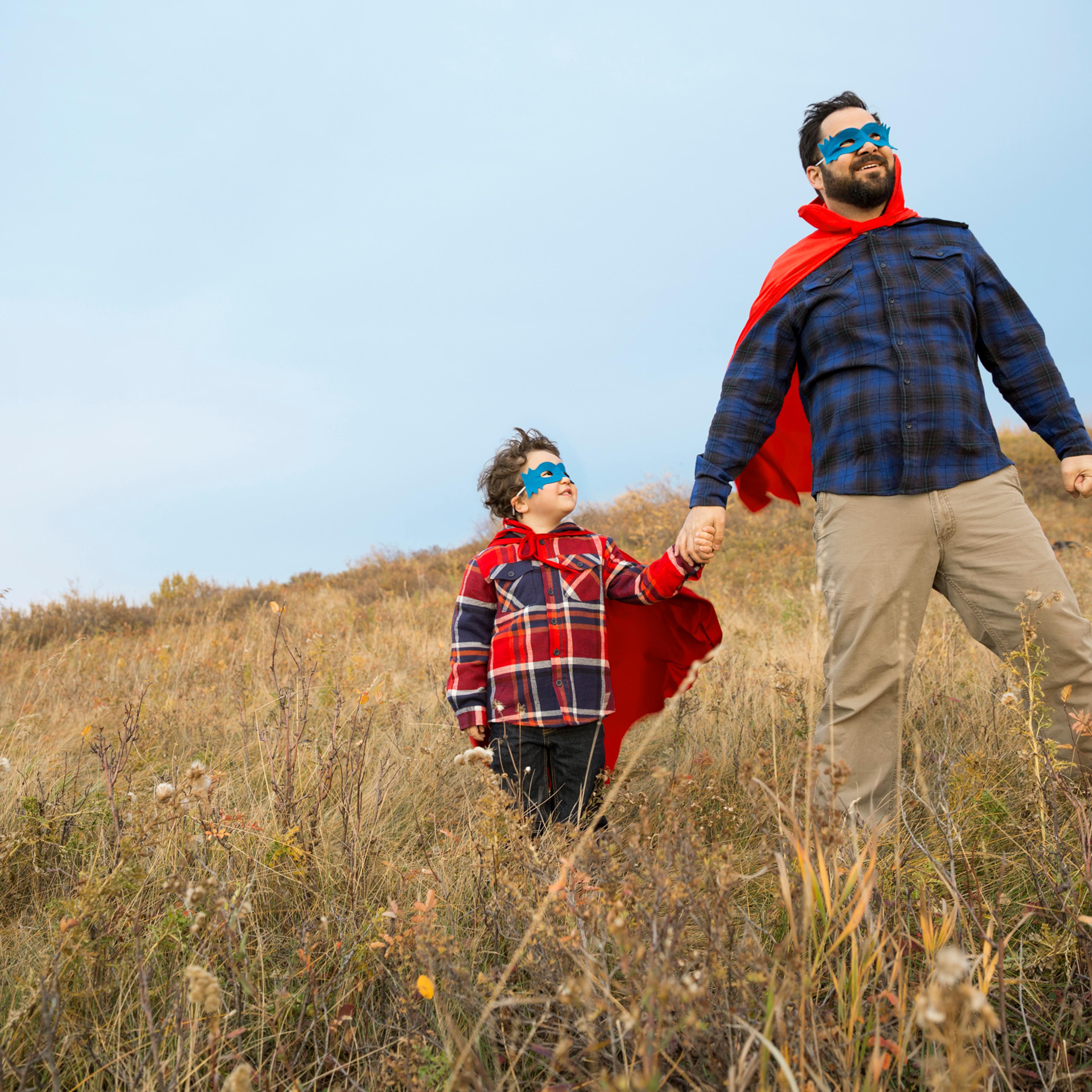 Father and son in superhero capes in field