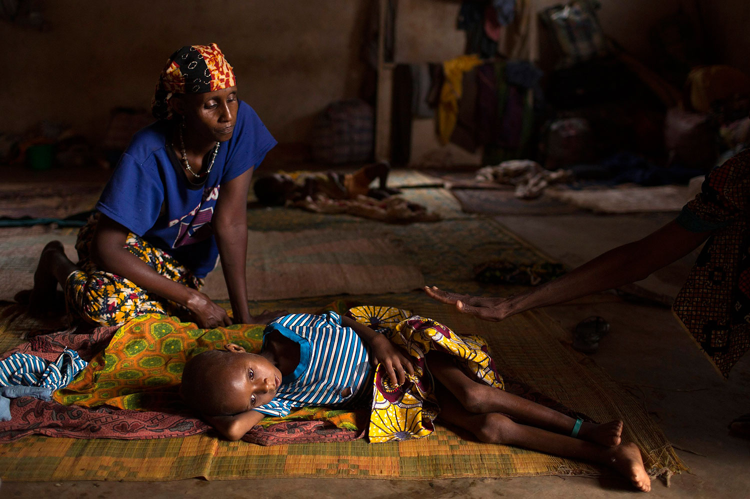 Relatives sit near Aliou Abalaye, 4, as he lies sick on the floor near  Kilometre 12