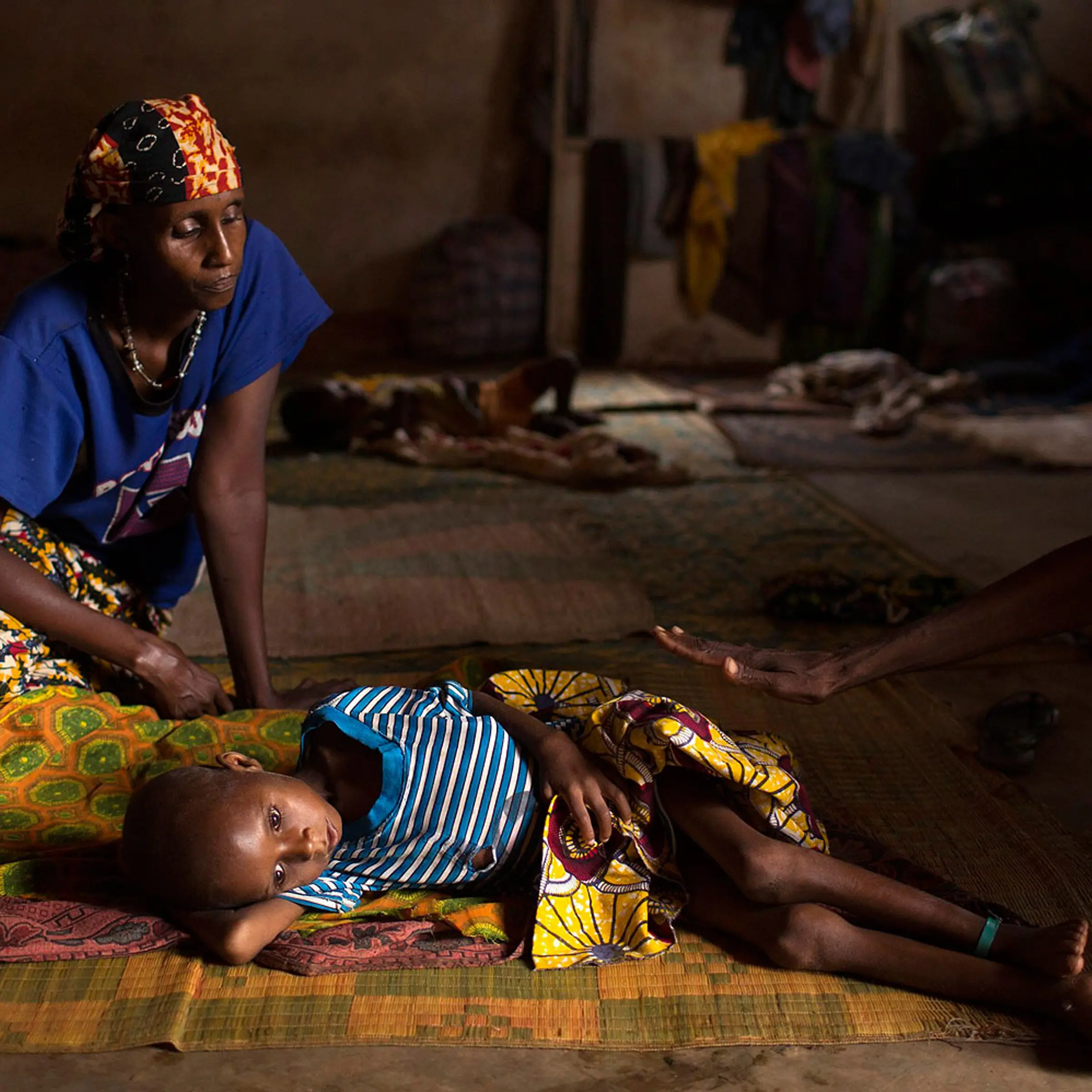 Relatives sit near Aliou Abalaye, 4, as he lies sick on the floor near Kilometre 12
