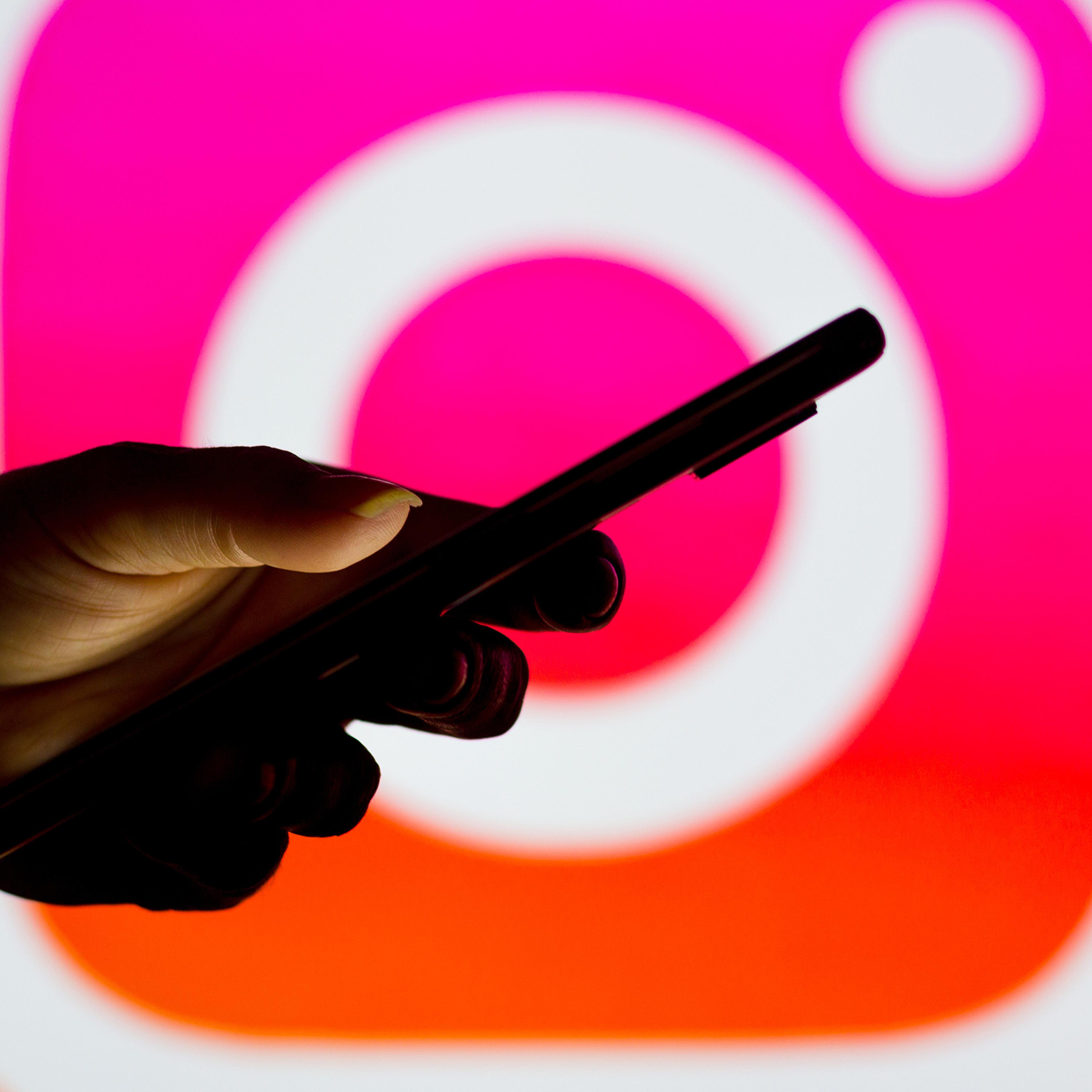 The Instagram logo seen in the background of a silhouette of a woman holding a mobile phone.