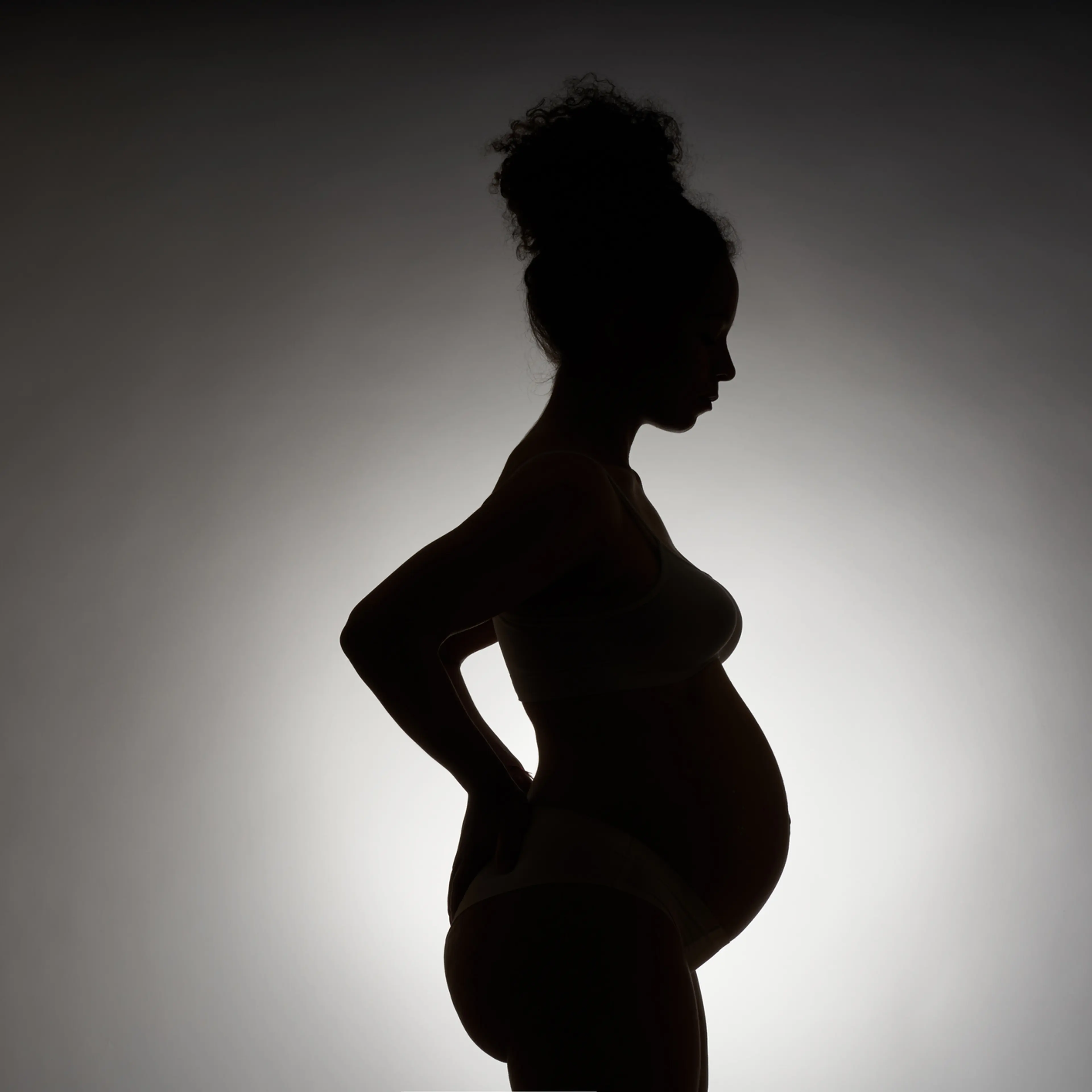 Silhouette of a pregnant African-American woman on a white background. The profile of a young woman with curly hair in a bump stands and holds her hands on her back. The concept of motherhood, pregnancy, back pain and childbirth.