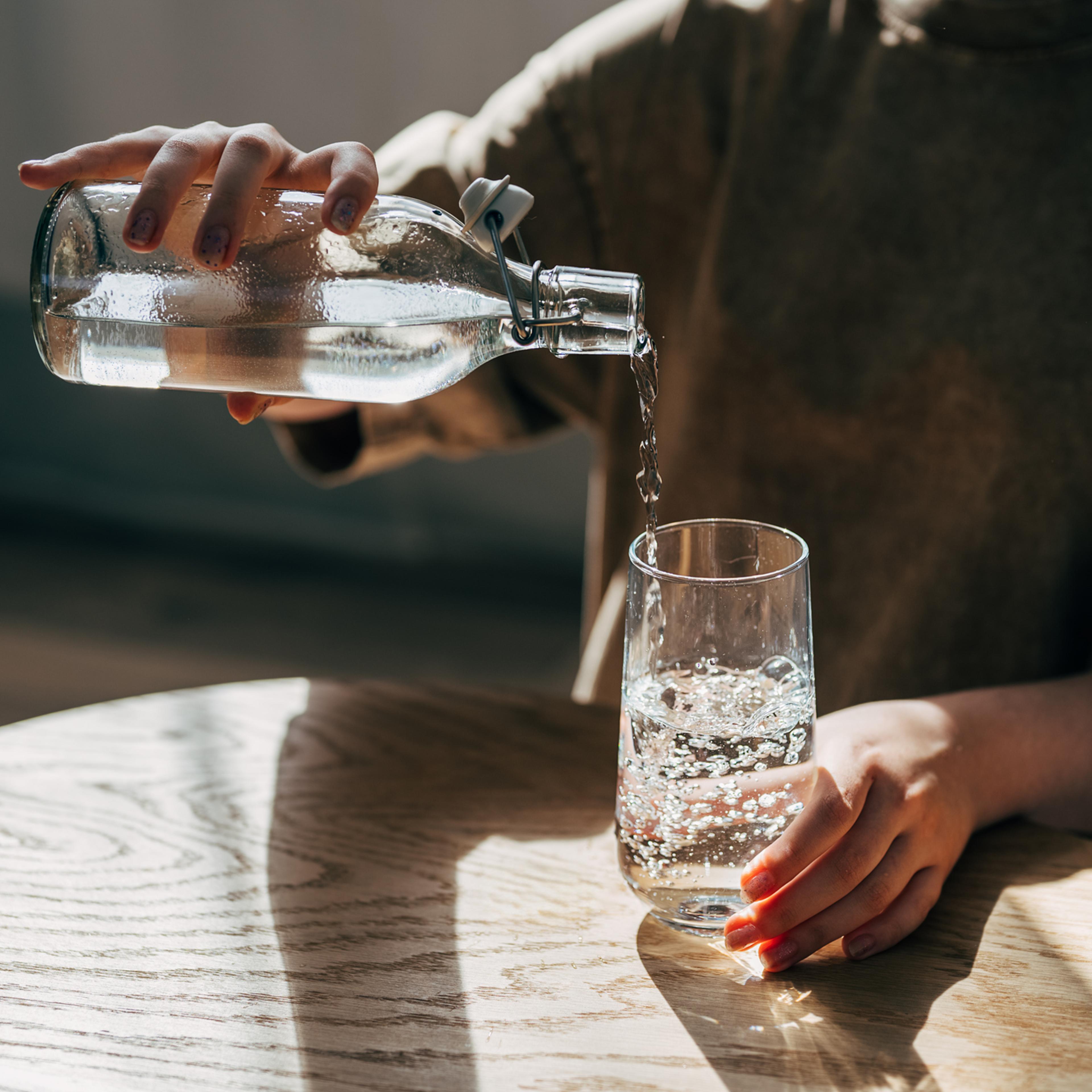 a woman at the table pours a glass of water from a bottle