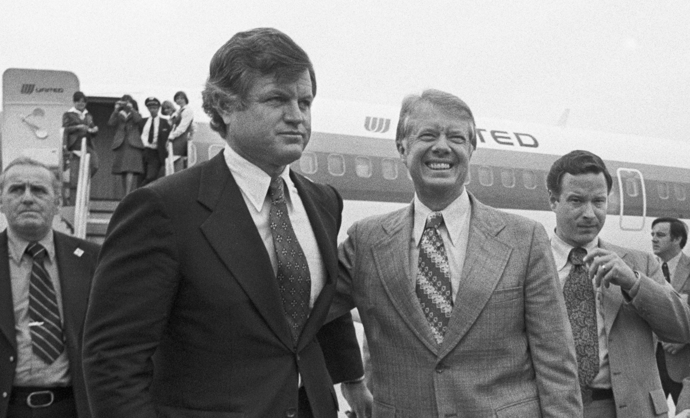 Pictured (center), Democratic presidential nominee Jimmy Carter, (R), puts his arm around Senator Edward M. Kennedy (L) as he arrived at Logan International Airport in Boston on Sep. 30, 1976, for a four-hour campaign blitz.