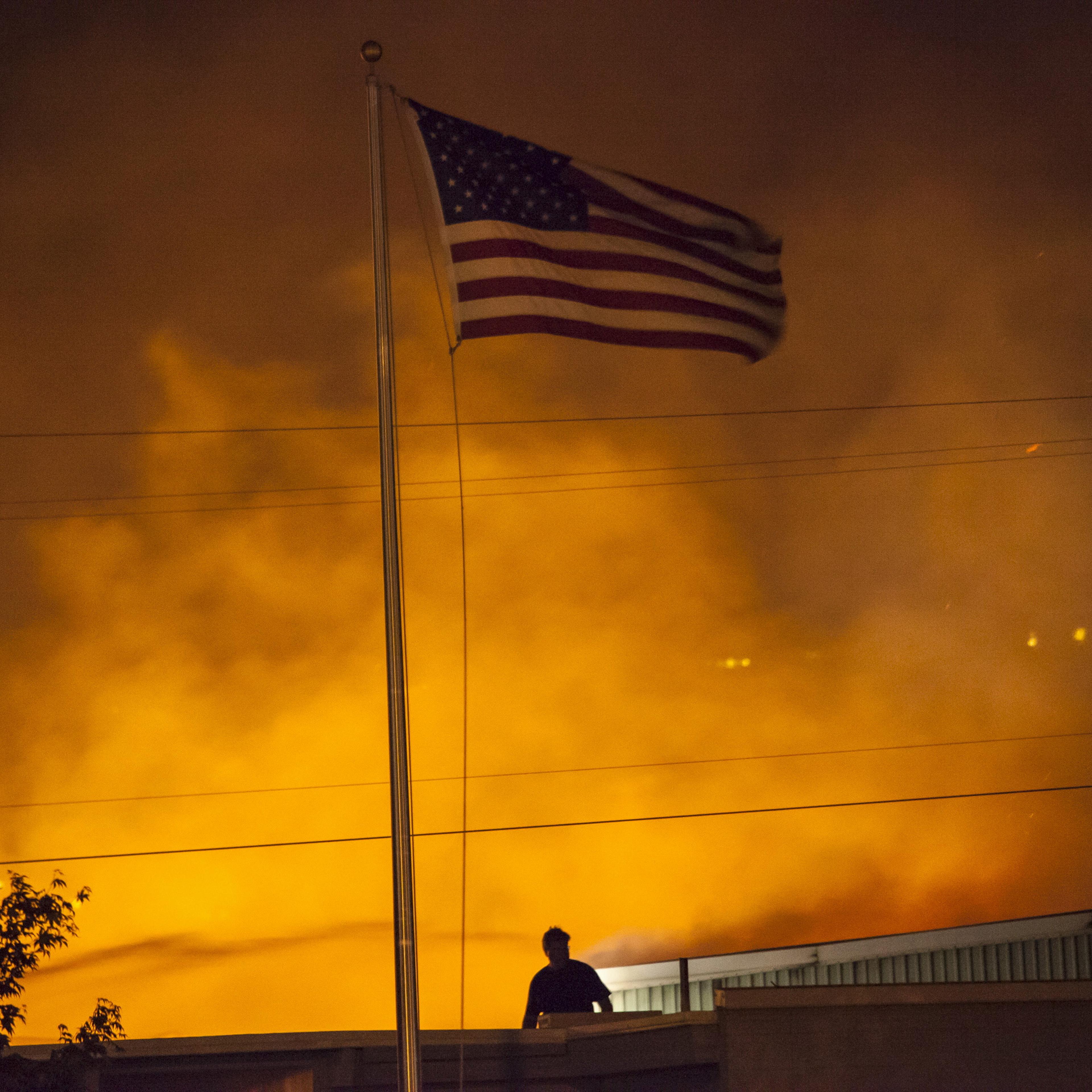 A U.S. flag is seen as a commercial building burns after being ignited by the Sleepy Hollow fire in Wenatchee, Washington