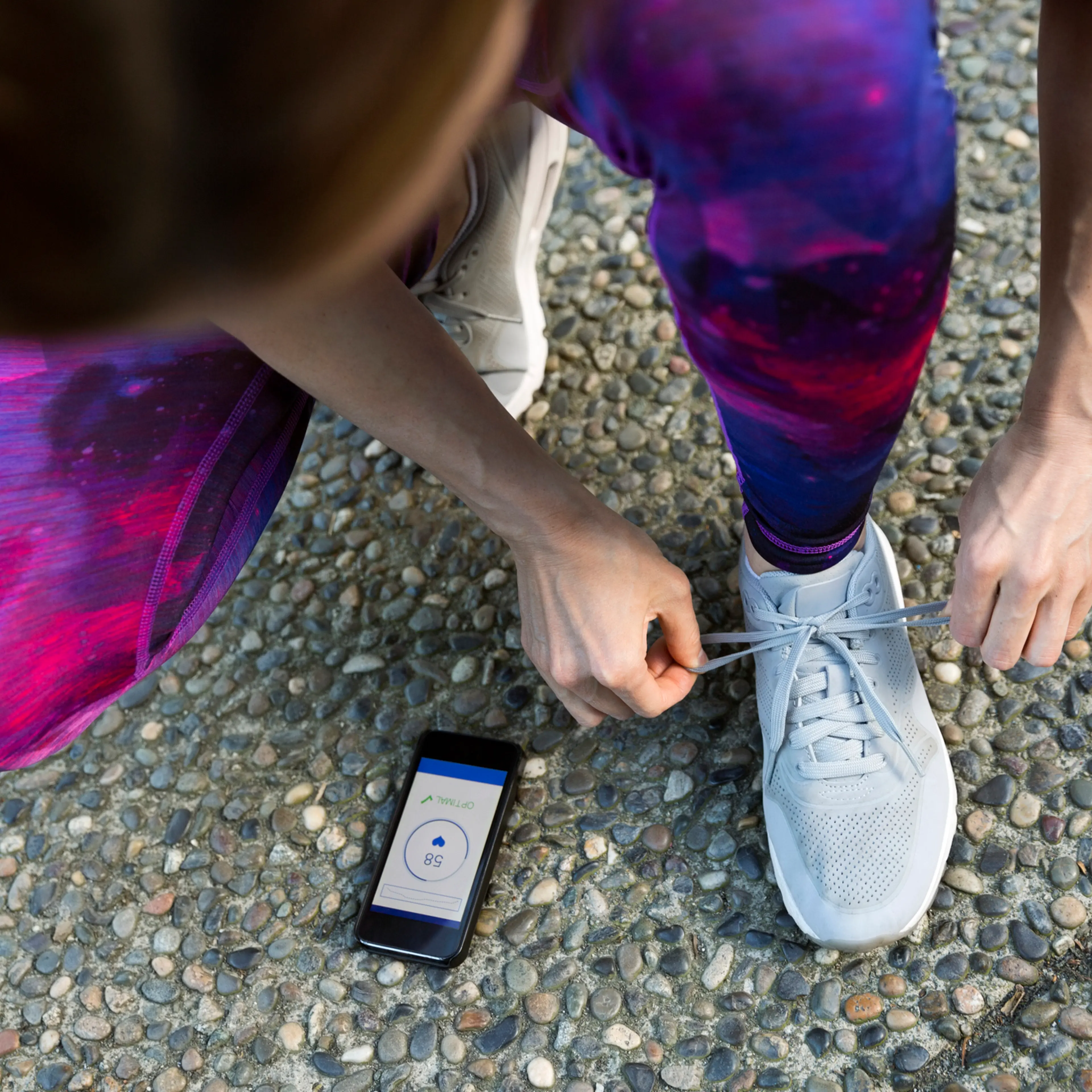 Runner tying shoe and checking heart rate app on cell phone