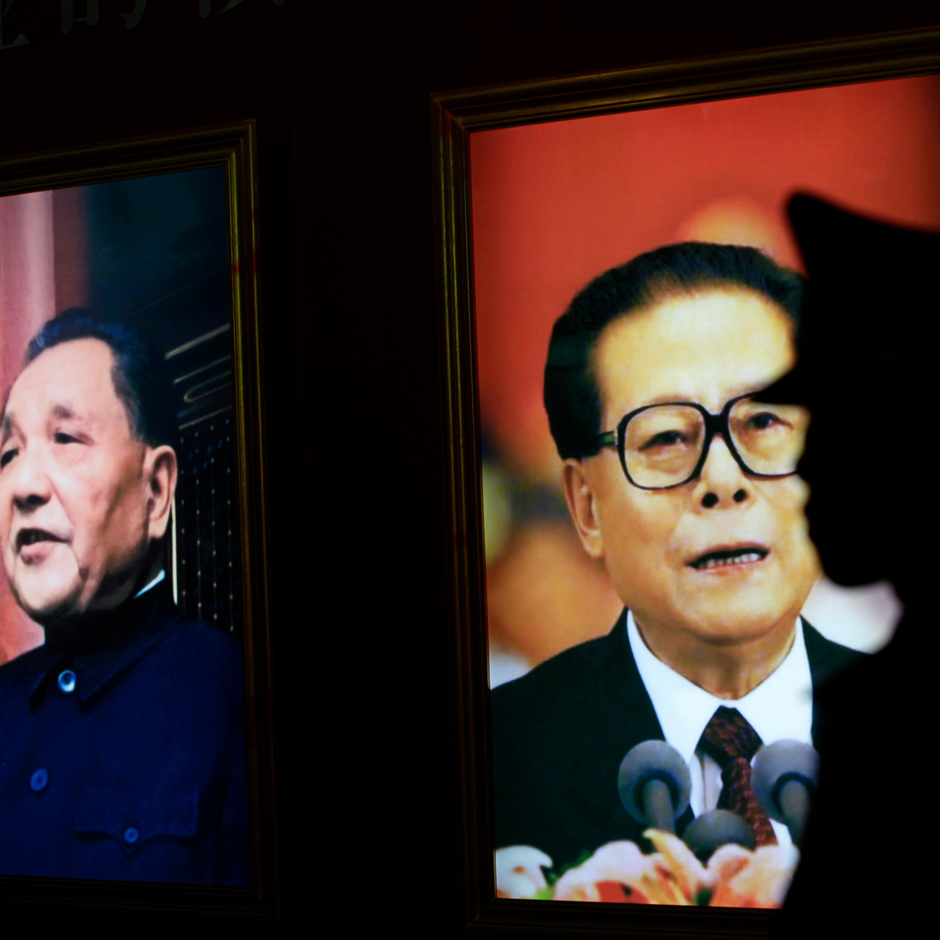 A security guard stands next to pictures of China's former President Jiang Zemin and late paramount leader Deng Xiaoping at an exhibition in Beijing
