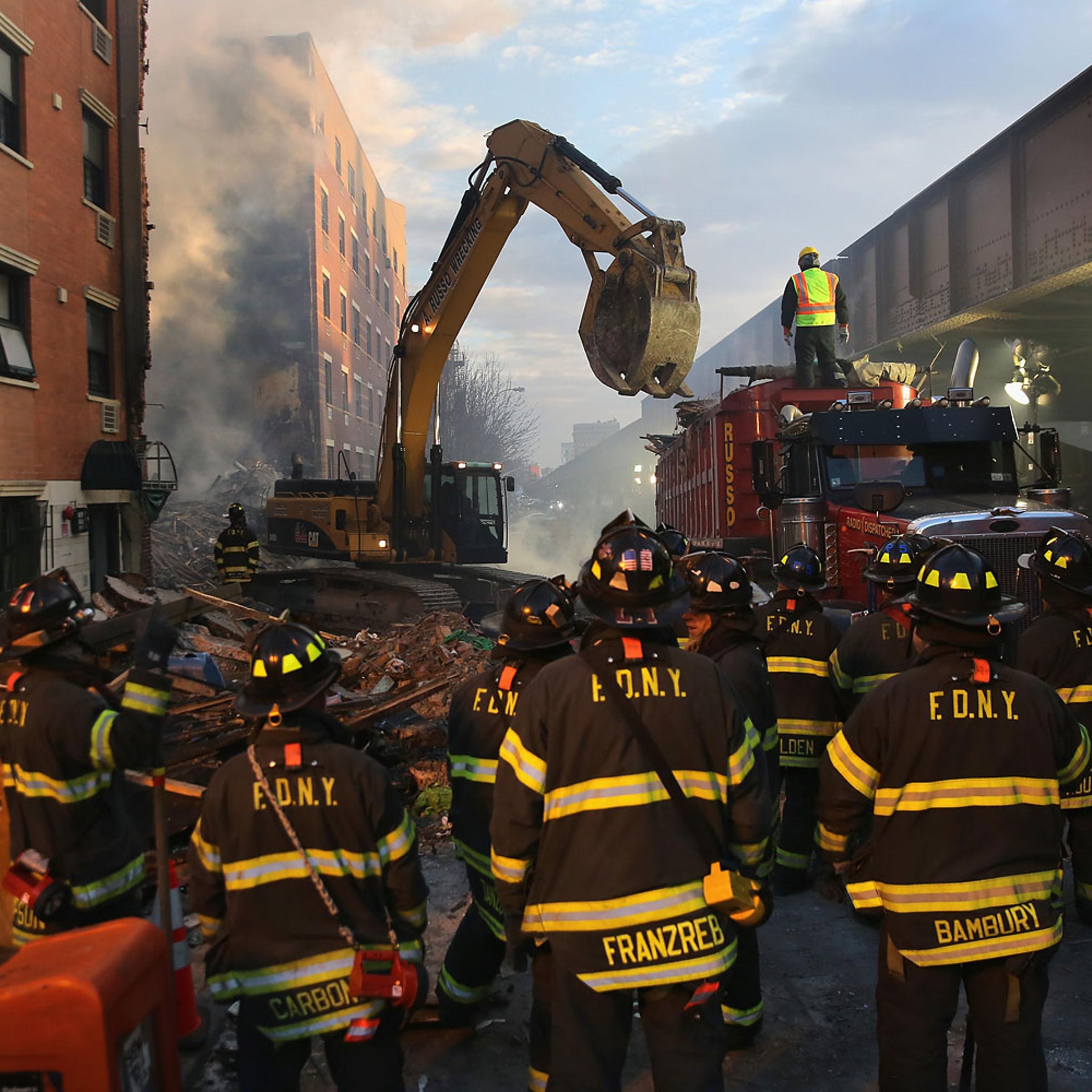 NEW YORK, NY - MARCH 13: Firemen watch as work crews remove debris from the site of an explosion in East Harlem on March 13, 2014 in New York City. At least 7 people were killed, according to reports, in Wednesday's explosion which collapsed two building
