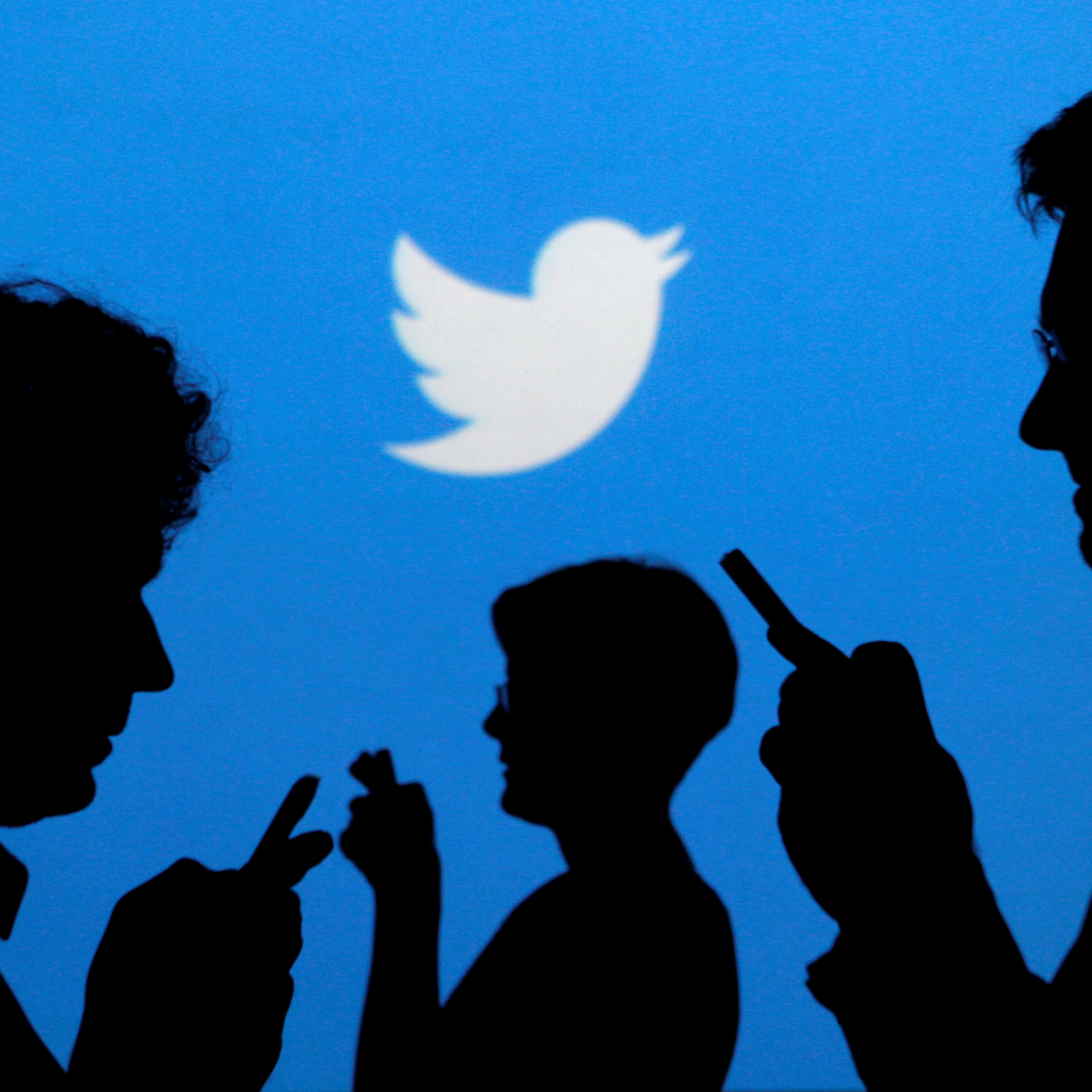 FILE PHOTO - People holding mobile phones are silhouetted against a backdrop projected with the Twitter logo in Warsaw