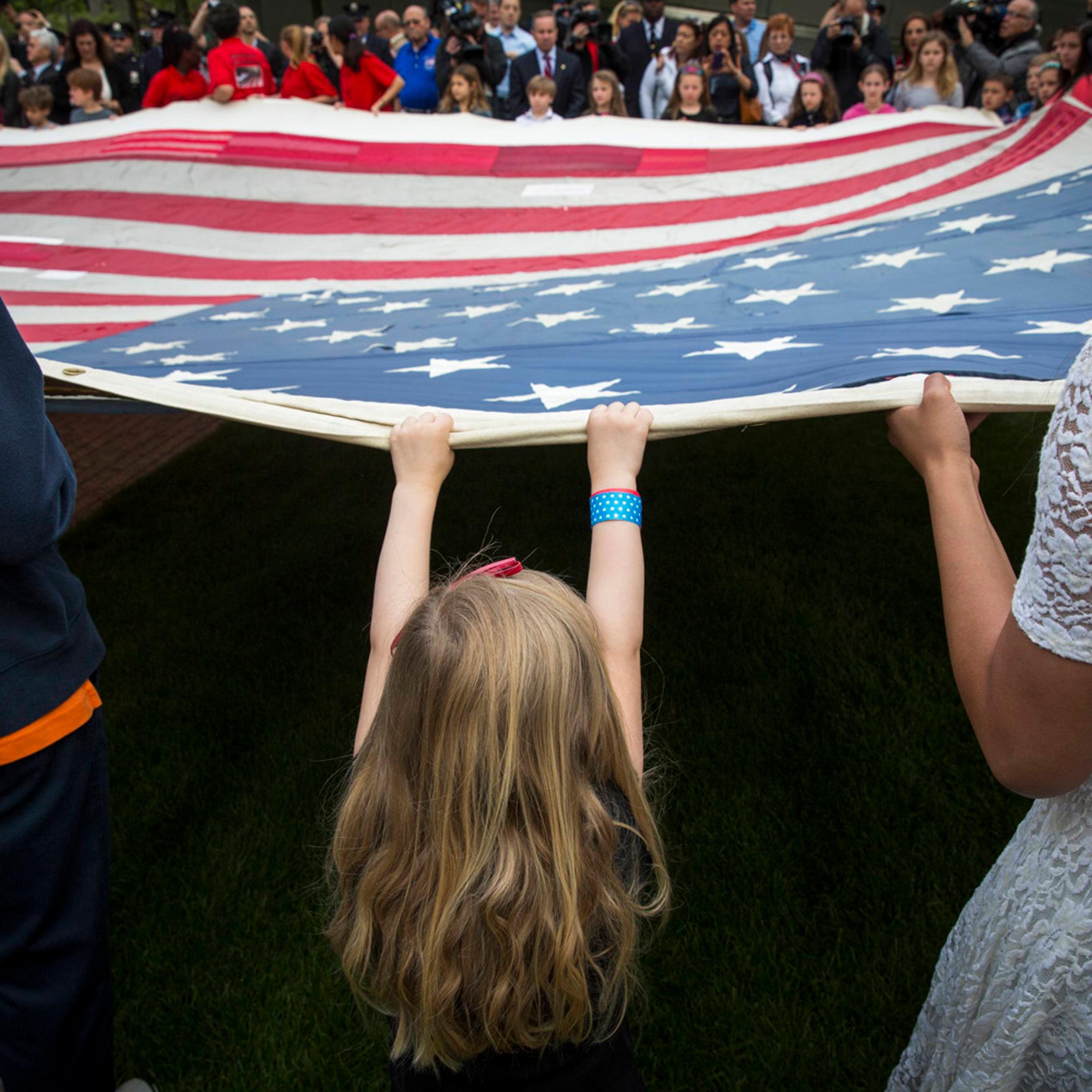 A girl designated to assist with transferring the National 9/11 Flag holds it aloft on the grounds of the 9/11 Memorial Plaza before donating it to the National September 11 Memorial Museum in New York